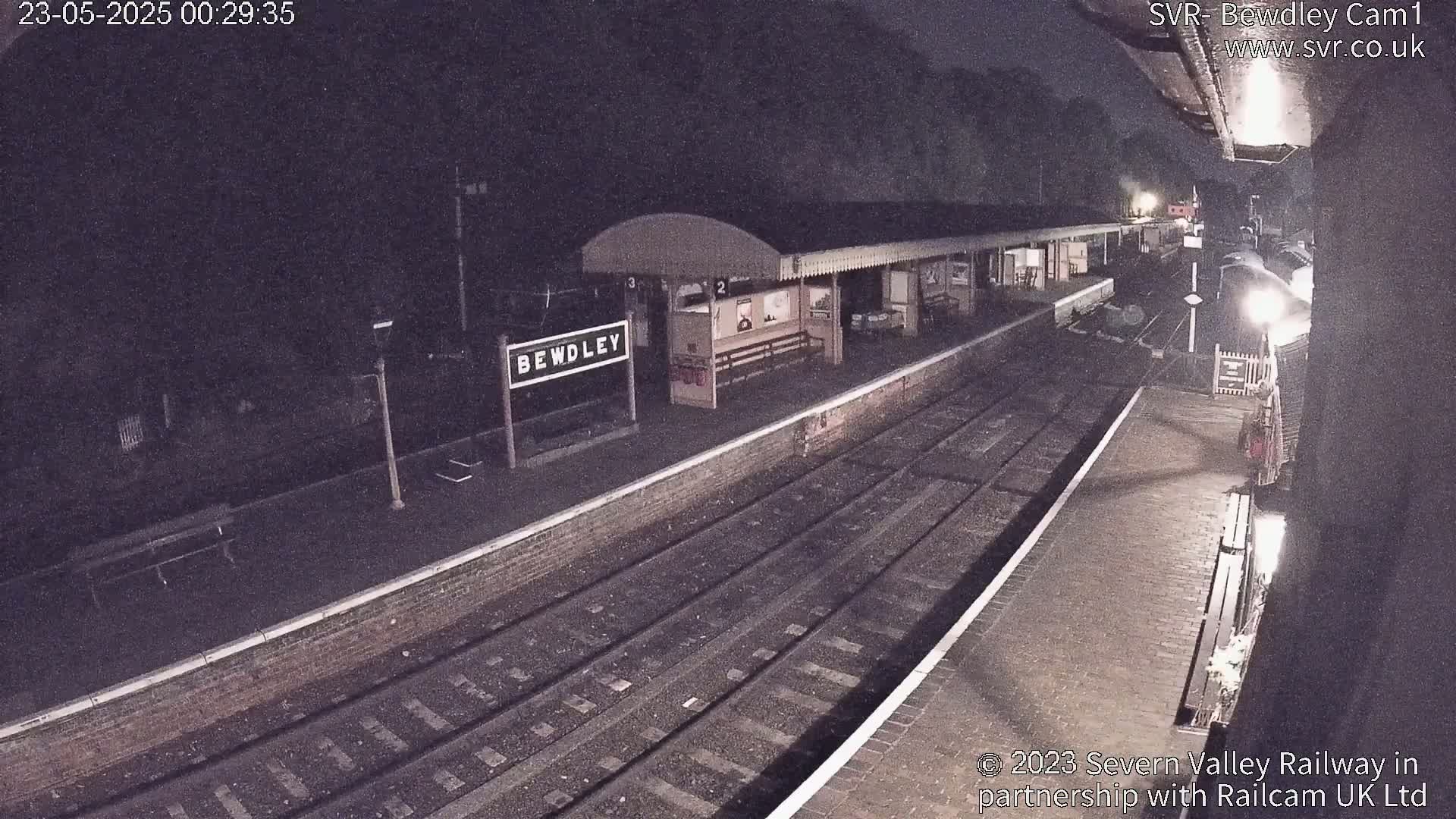 A nighttime view of a train station platform with train tracks and a partially visible train.