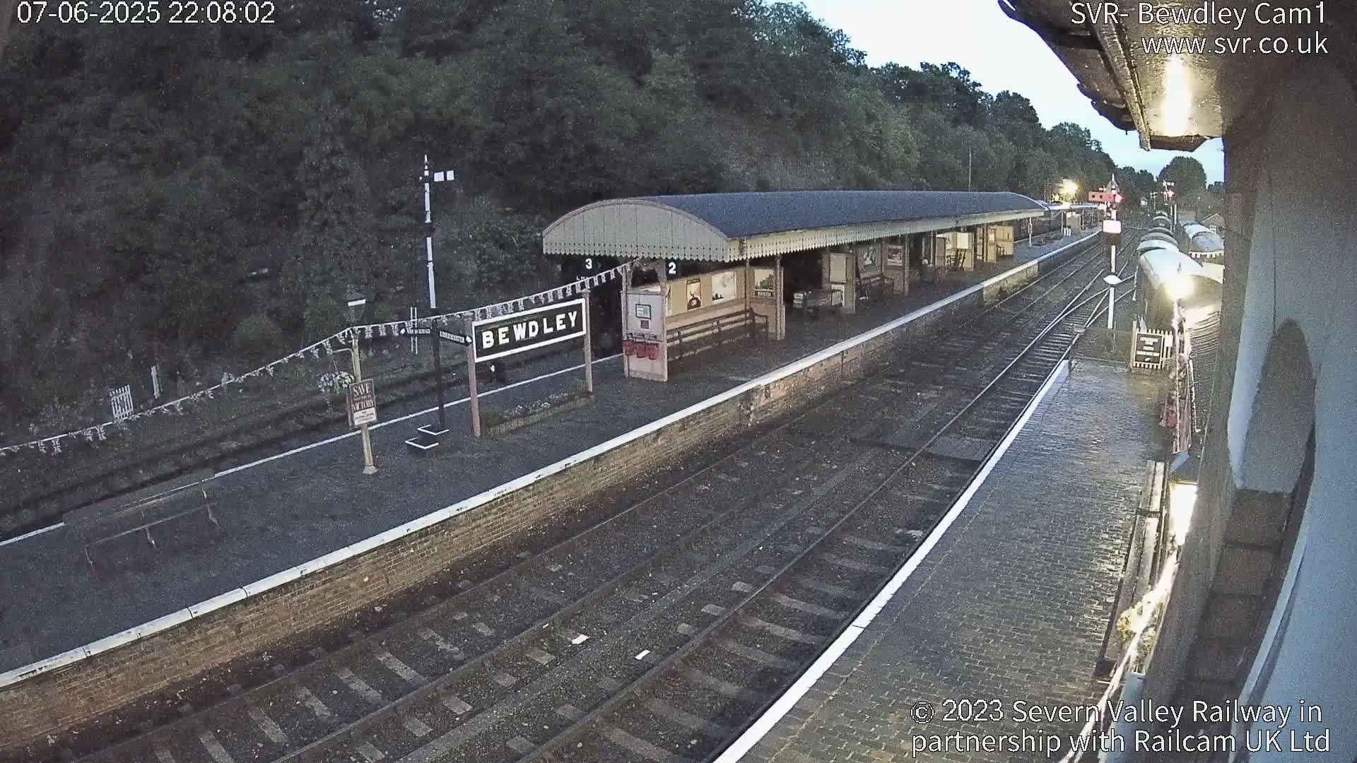 A mostly empty train station at night, with a covered platform and train tracks extending into the darkness.