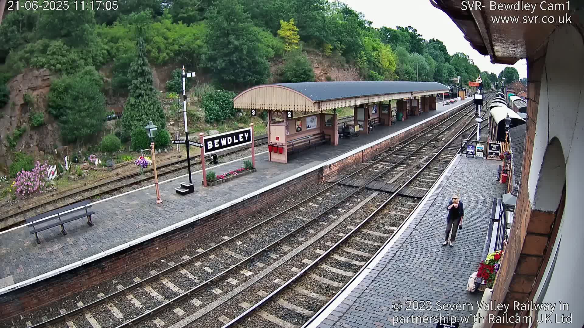 A train platform with a covered waiting area and several tracks is seen on a partly sunny day.