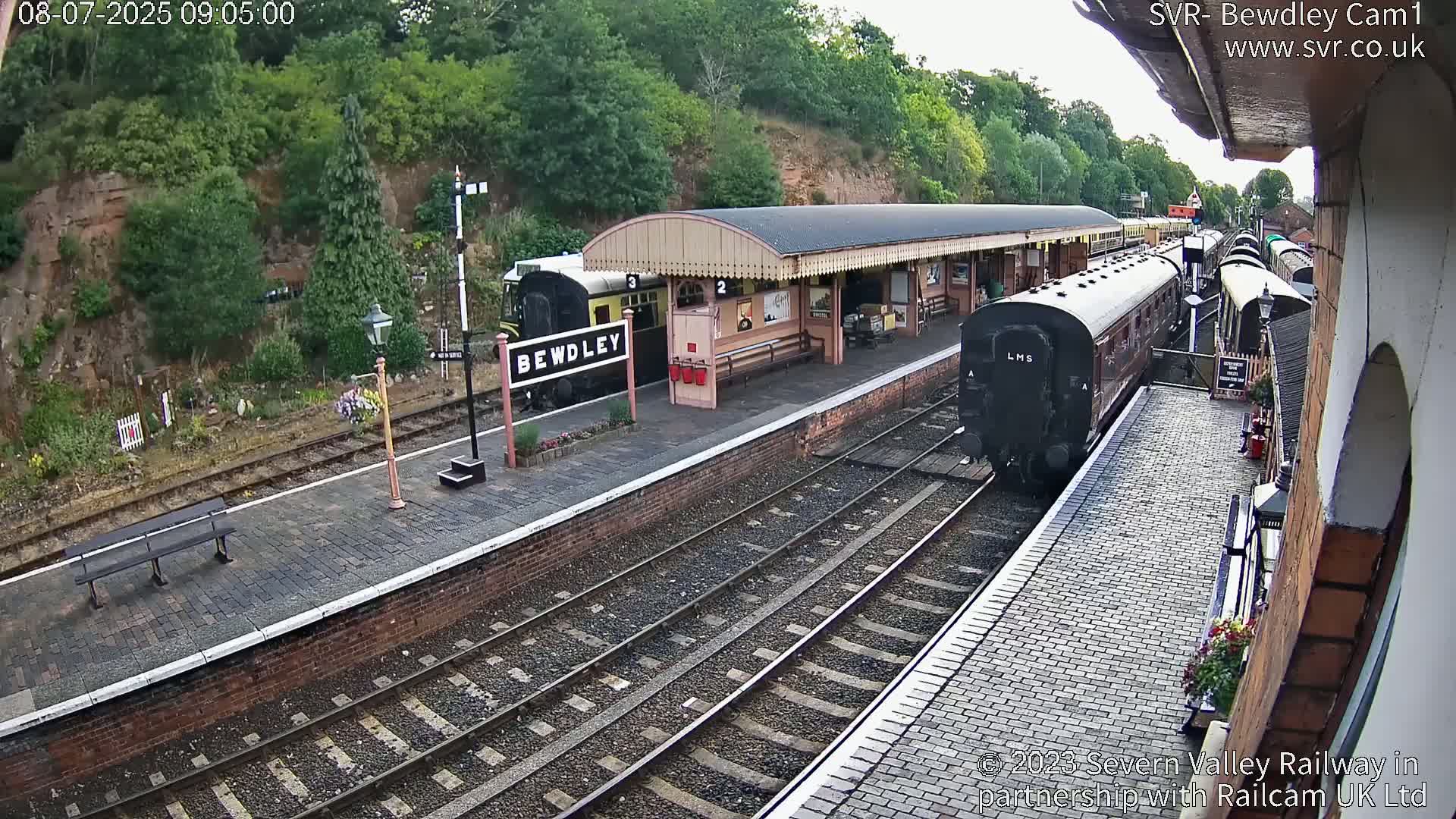 A train is pulling into a railway station platform on a partly cloudy day.
