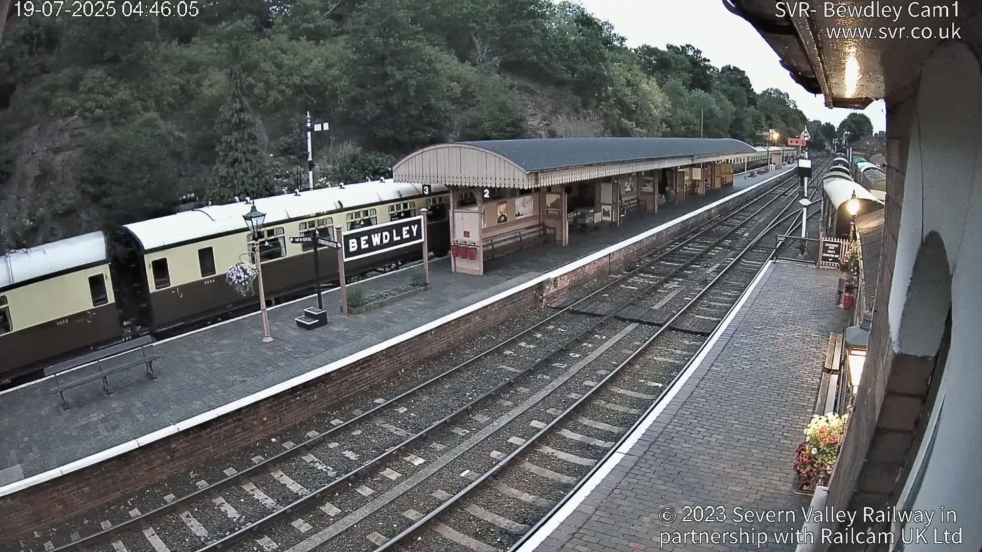 A train sits at a railway station platform under an overcast sky.