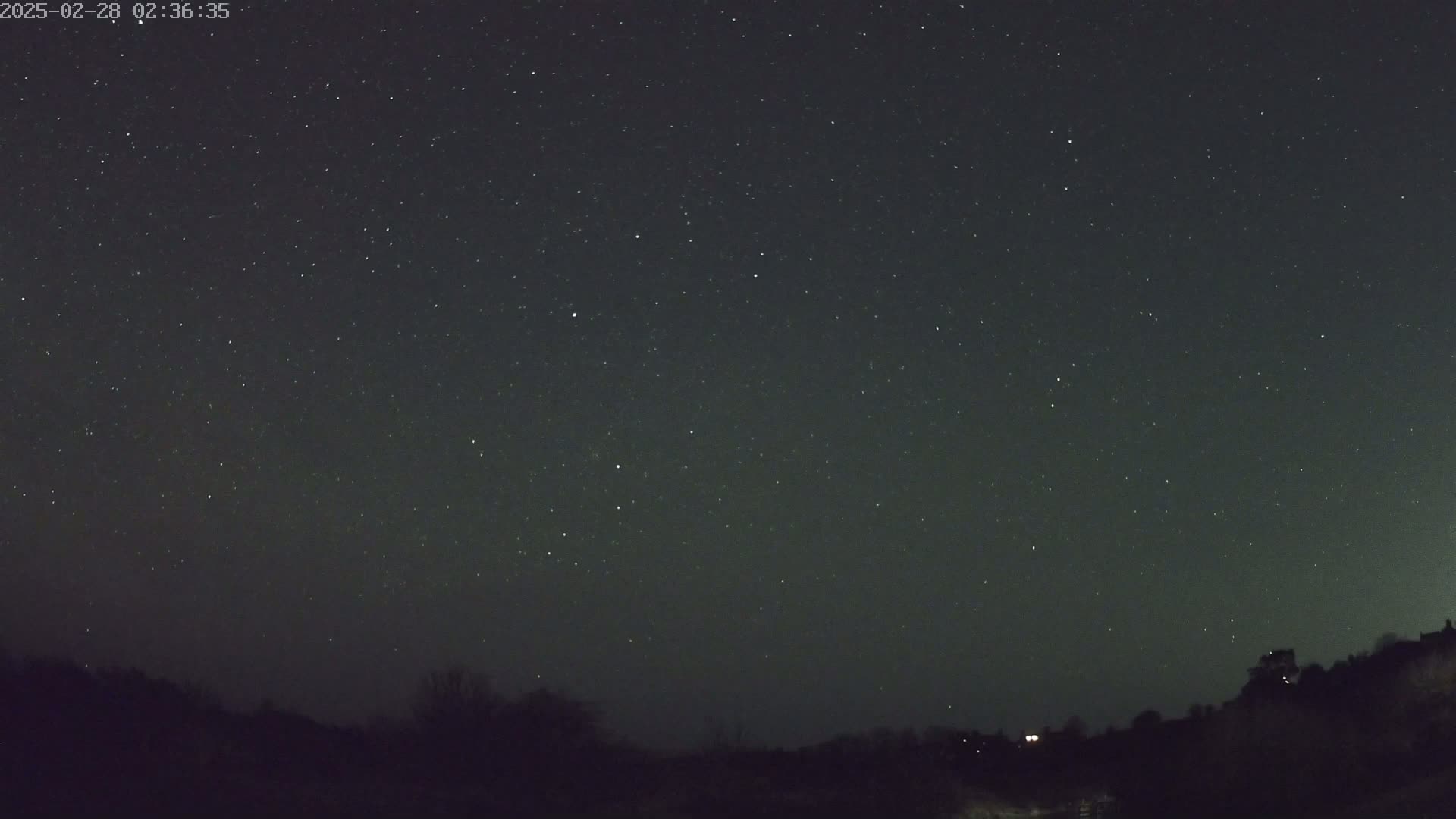 A nighttime scene shows a dark, star-filled sky above a silhouetted hilly landscape.