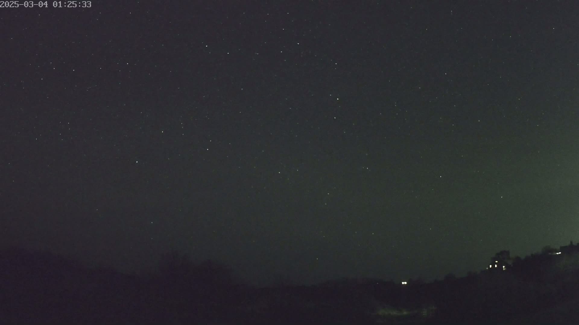 A nighttime outdoor scene shows a dark sky filled with stars above a silhouetted landscape with a few distant lights.