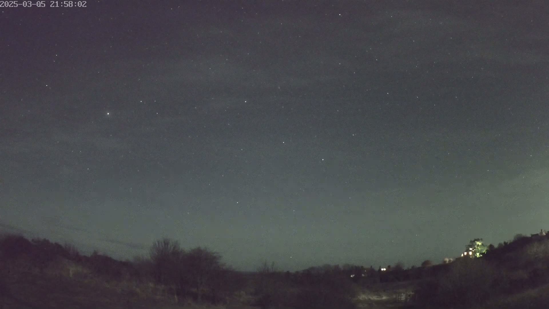 A night sky filled with stars overlooks a dark, treeline landscape.