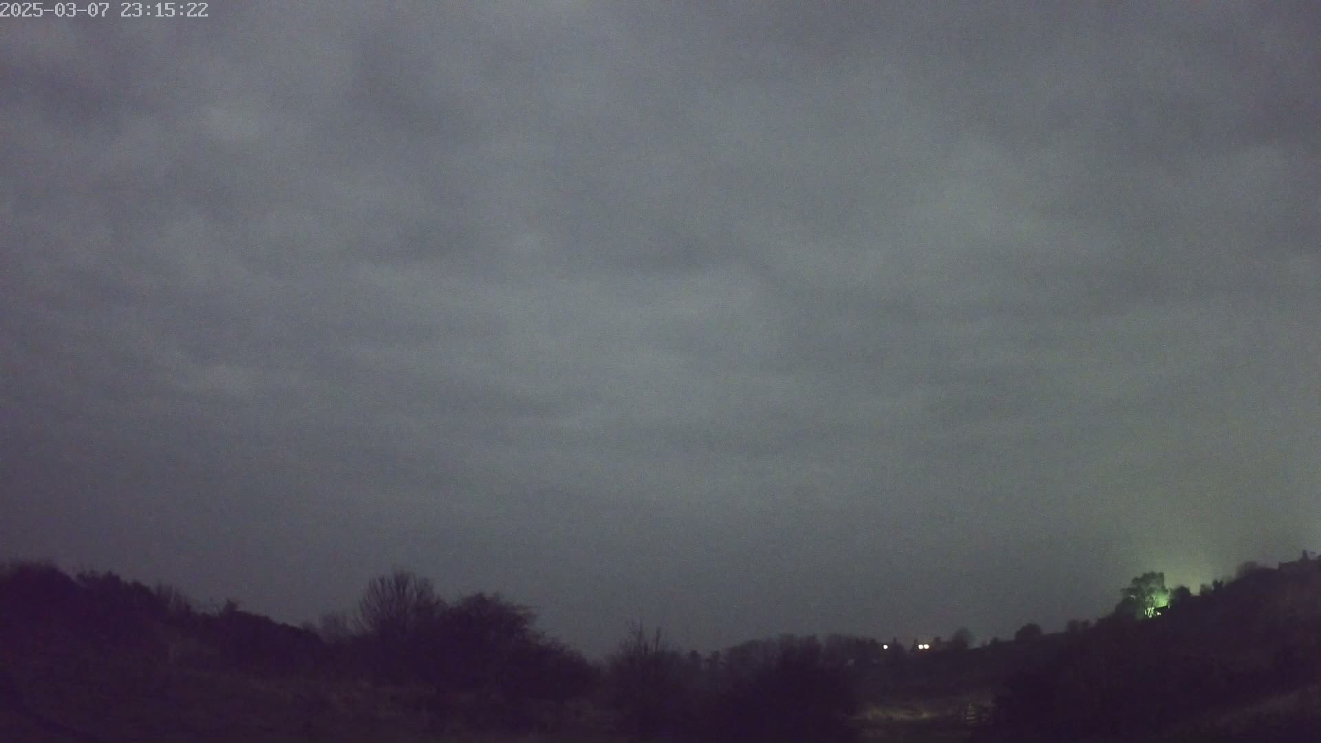 A dark, overcast night sky looms over a silhouetted landscape of trees and hills.