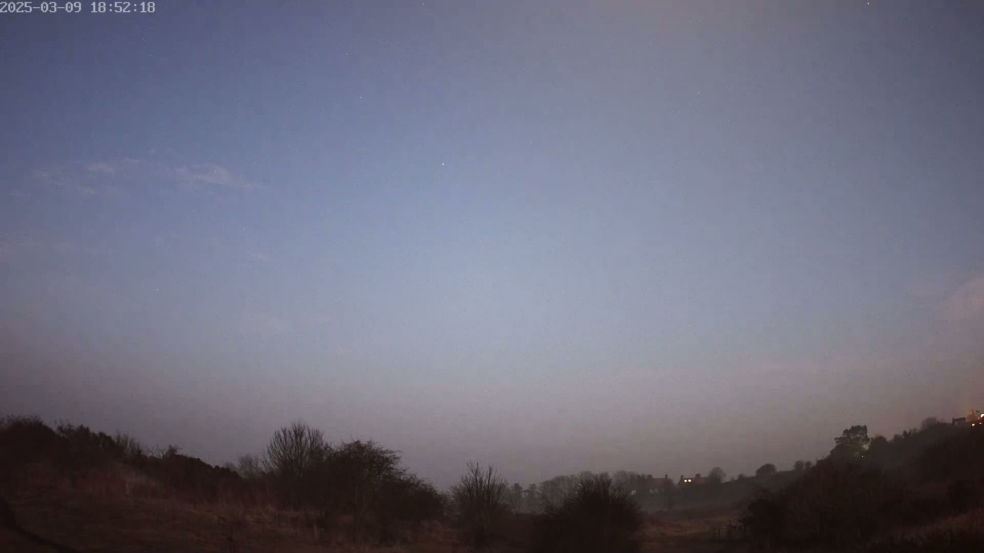 A dusky, hazy twilight sky hangs over a low-lying, barren landscape of dark shrubs and trees.