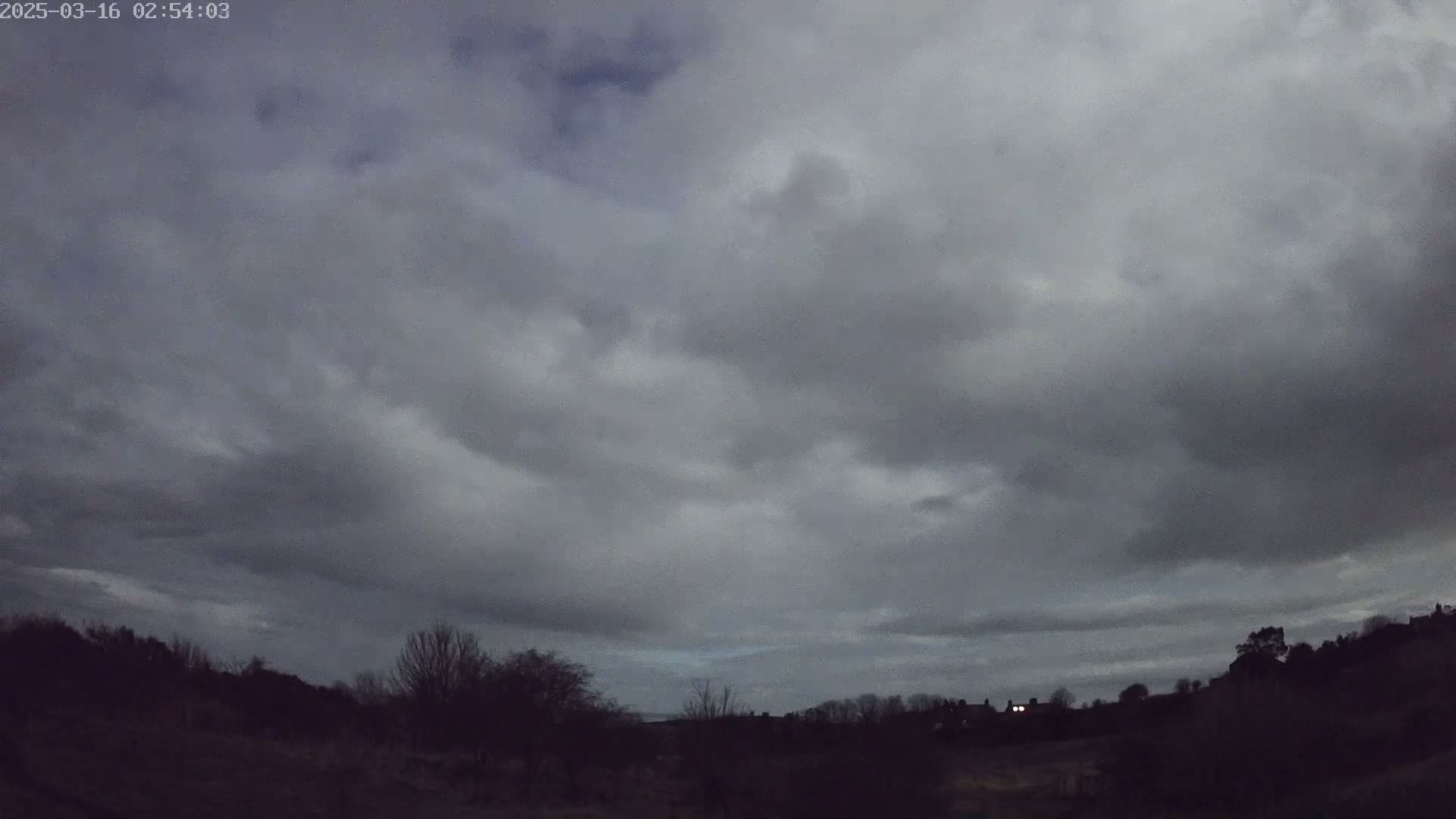 A mostly cloudy, dark sky over a silhouetted landscape of trees and buildings at twilight.