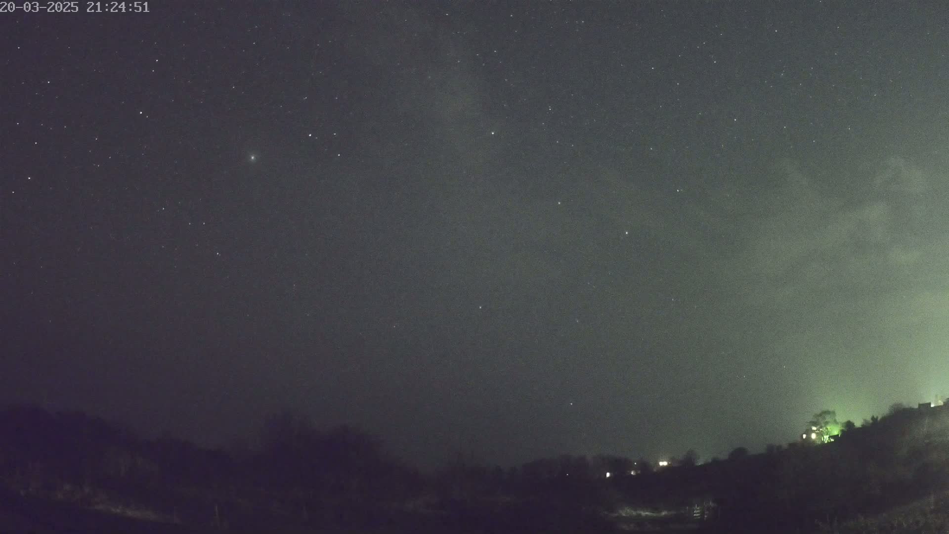 A nighttime long shot shows a mostly clear, dark sky filled with stars above a dark, silhouetted tree line.