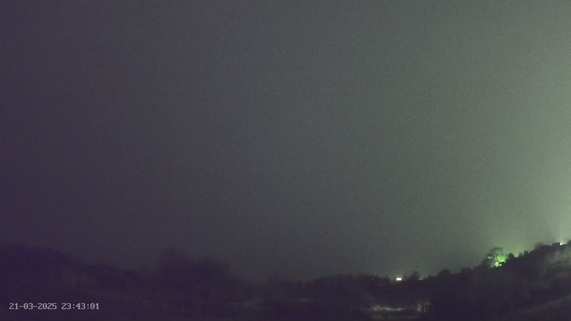 A nighttime, foggy landscape shows a dark hill silhouetted against a gray sky.