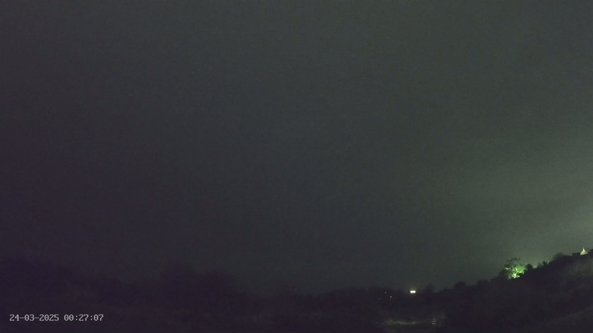 A dark, nighttime scene shows a mostly overcast sky above a low-lying, silhouetted landscape.