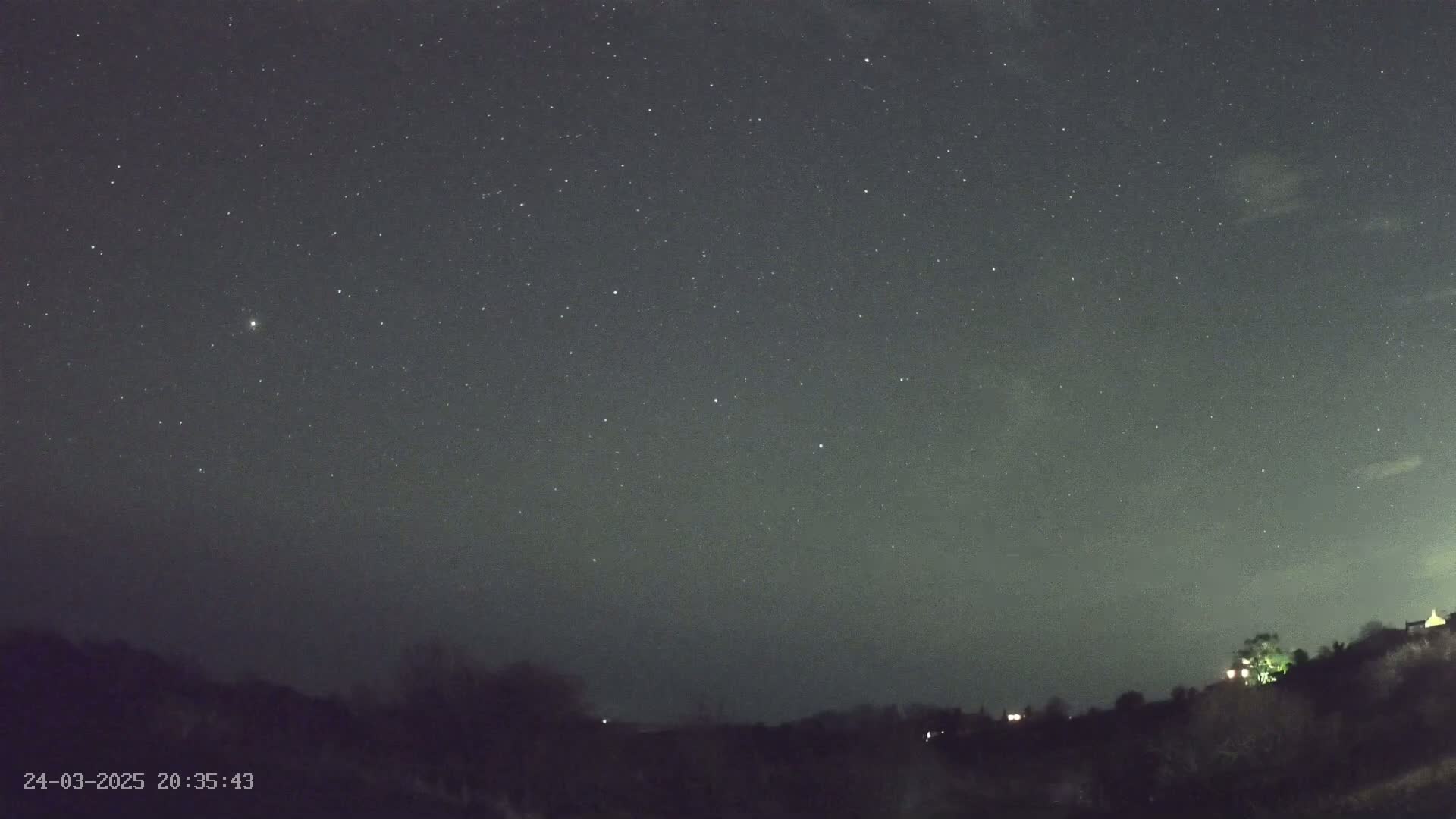 A night sky filled with stars is visible above a dark, silhouetted landscape of trees and buildings.