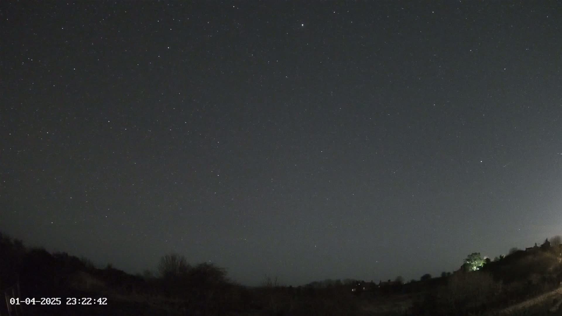 A night sky filled with stars over a dark, hilly landscape.