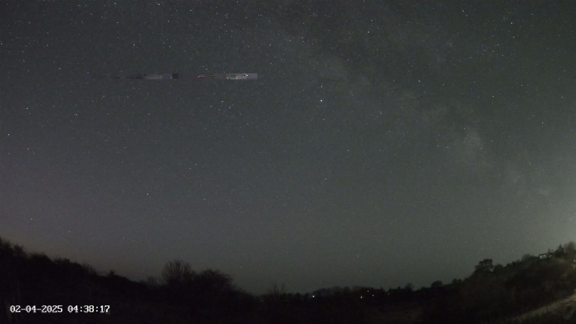 A night sky filled with stars and the Milky Way is visible above a dark, silhouetted treeline.