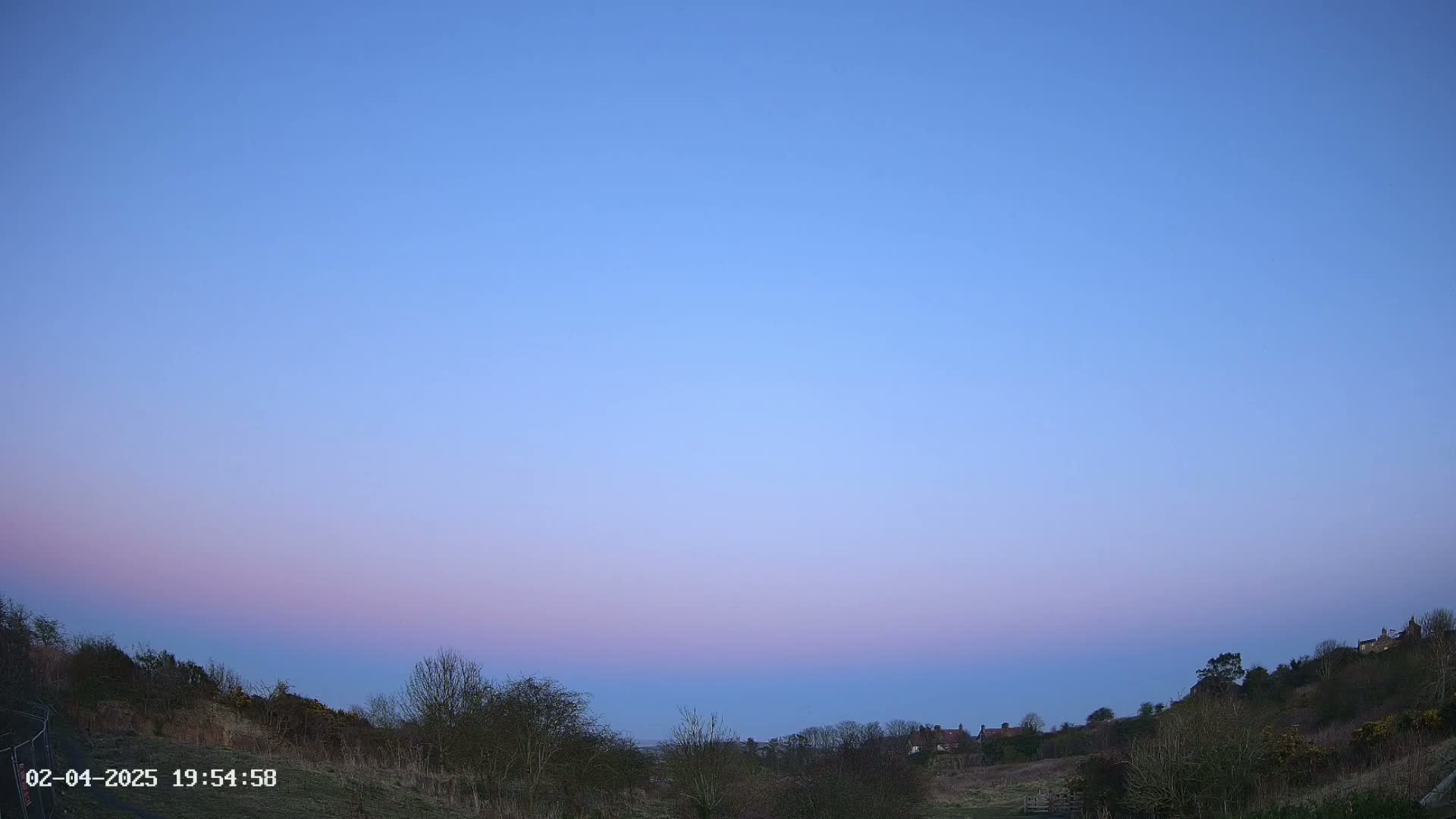 A pale pink and blue twilight sky over a landscape of low hills and sparse trees.