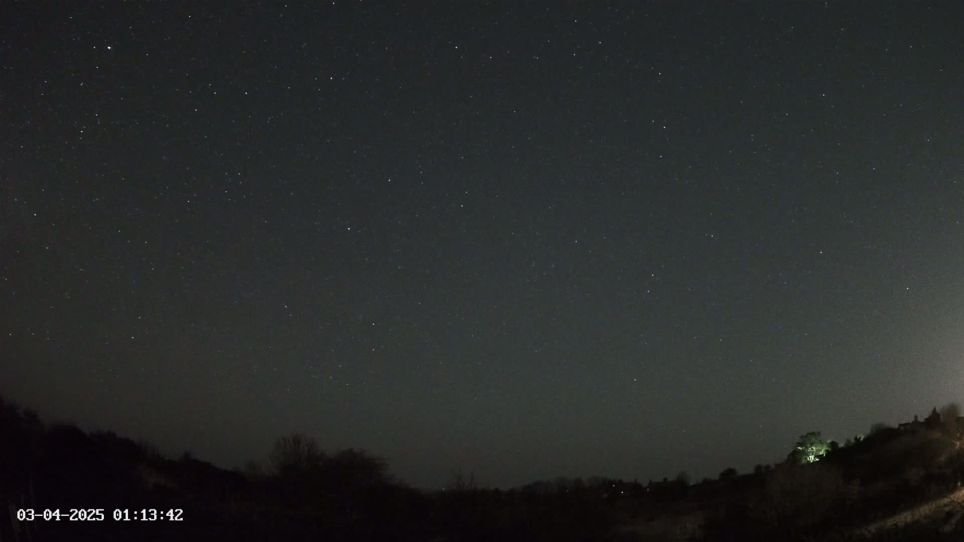 A nighttime view of a starlit sky over a dark, hilly landscape.