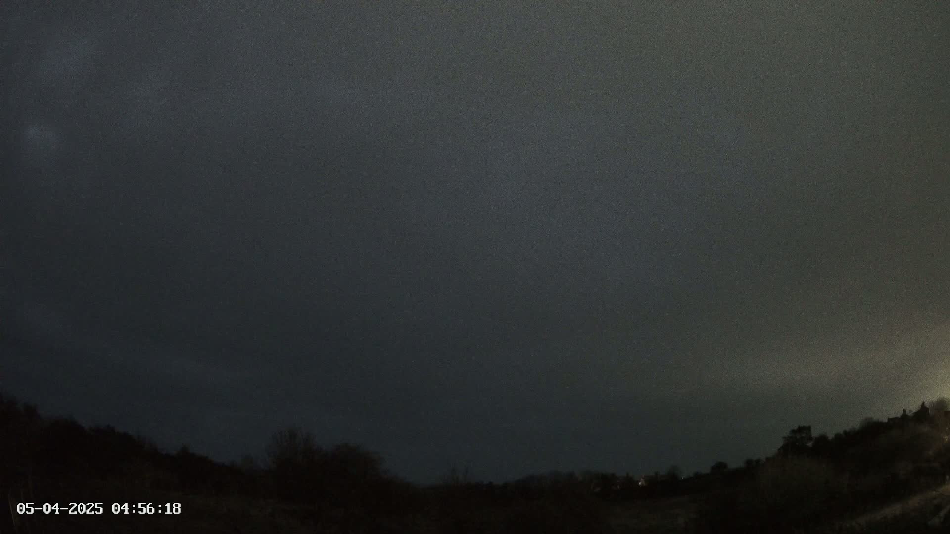 A dark, overcast night sky looms over a silhouetted landscape of trees and hills.