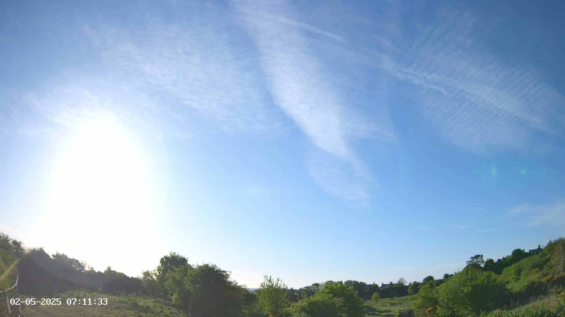 A mostly sunny day with wispy clouds overhead and green vegetation in the foreground.