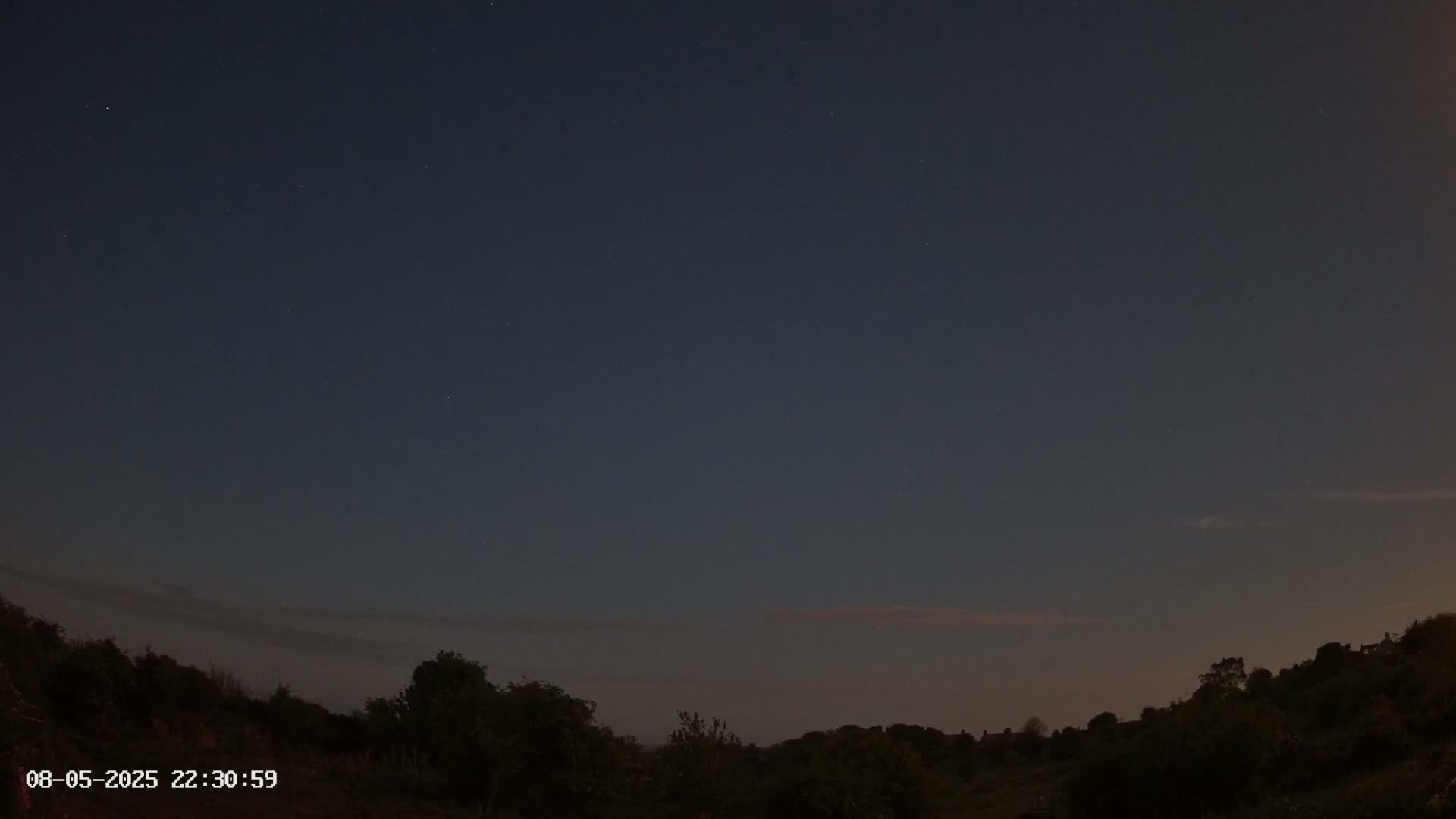 A dark, night sky with a few visible stars shows above a silhouetted line of trees and hills.