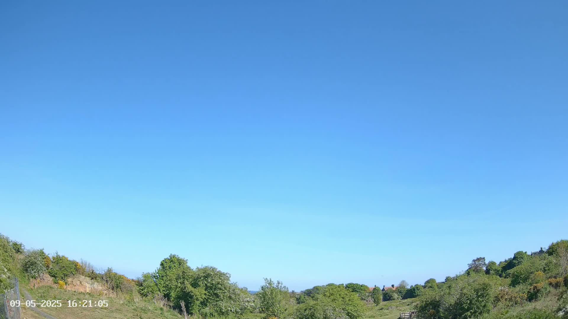 Under a clear blue sky, green hillsides meet in a valley with a few buildings visible in the distance.