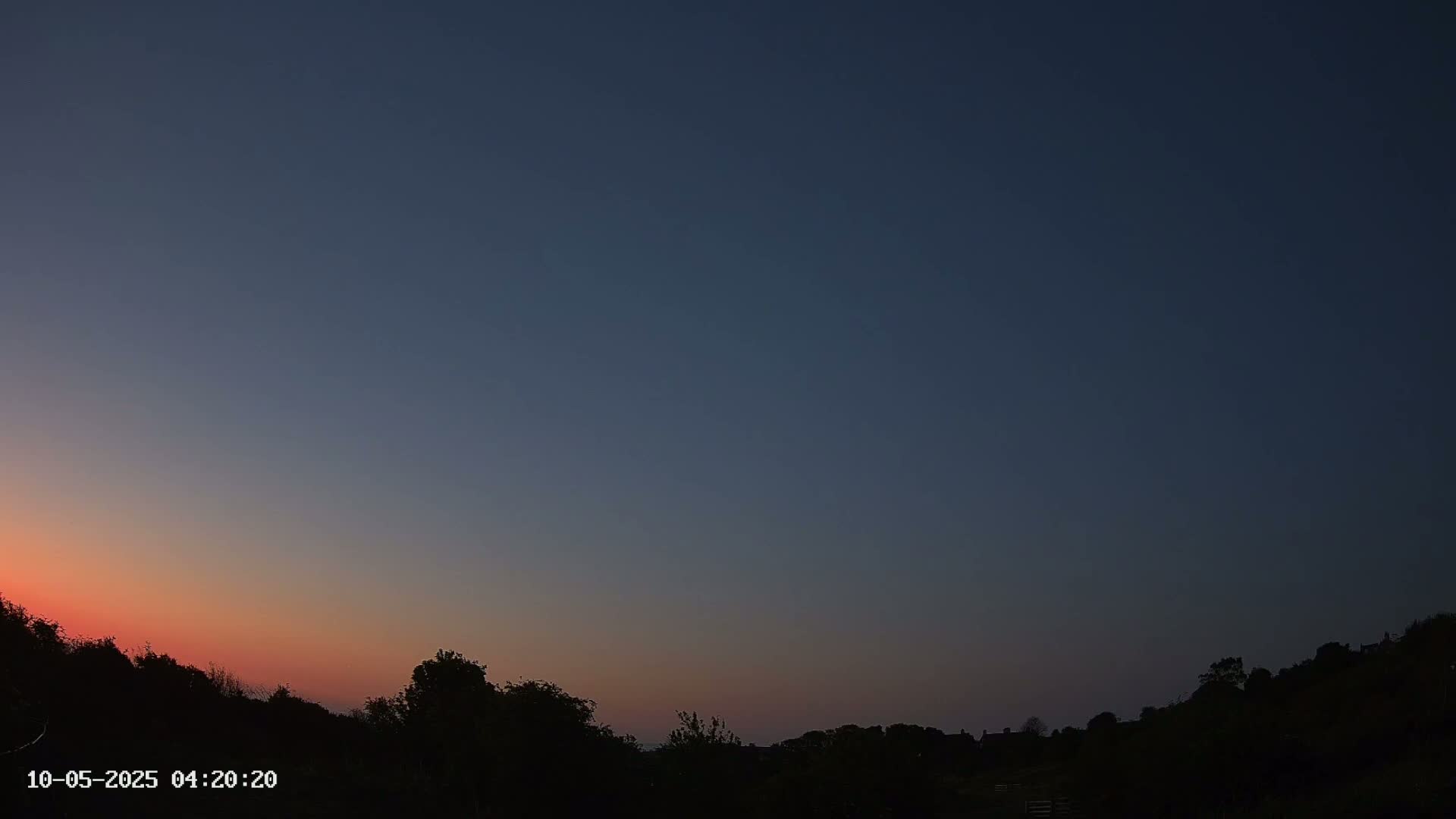 Silhouetted trees and a distant horizon are visible against a twilight sky with a pinkish-orange hue near the horizon and darkening to deep blue above.