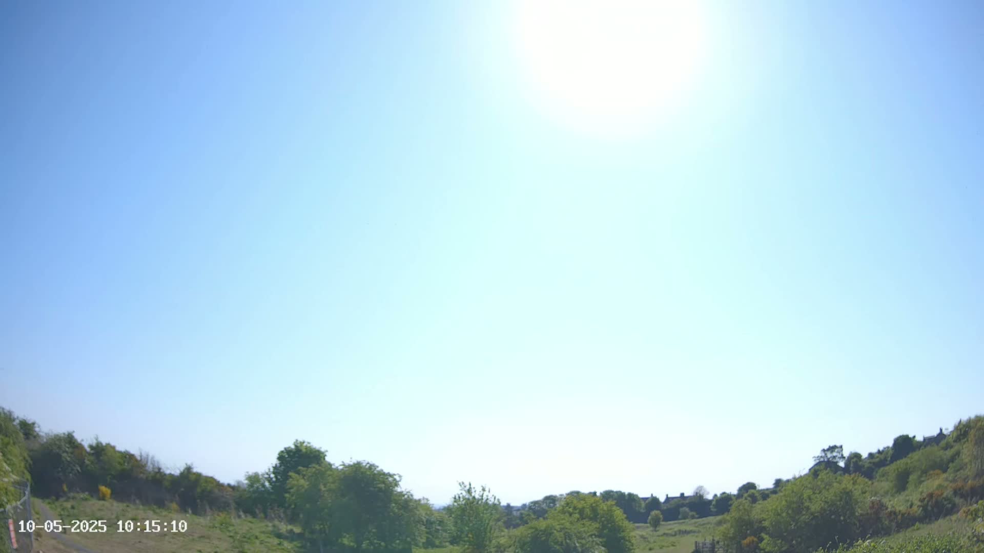 Under a bright, sunny sky, green hills and trees stretch across a landscape.