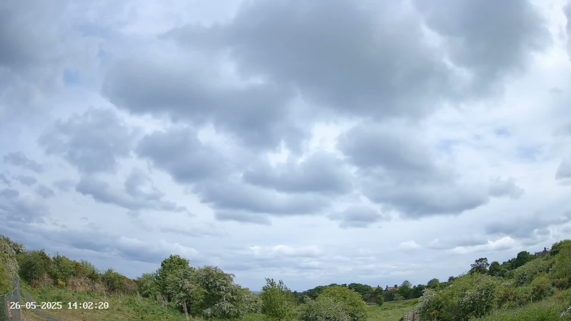 A mostly cloudy sky hangs over a verdant landscape with low hills and trees.