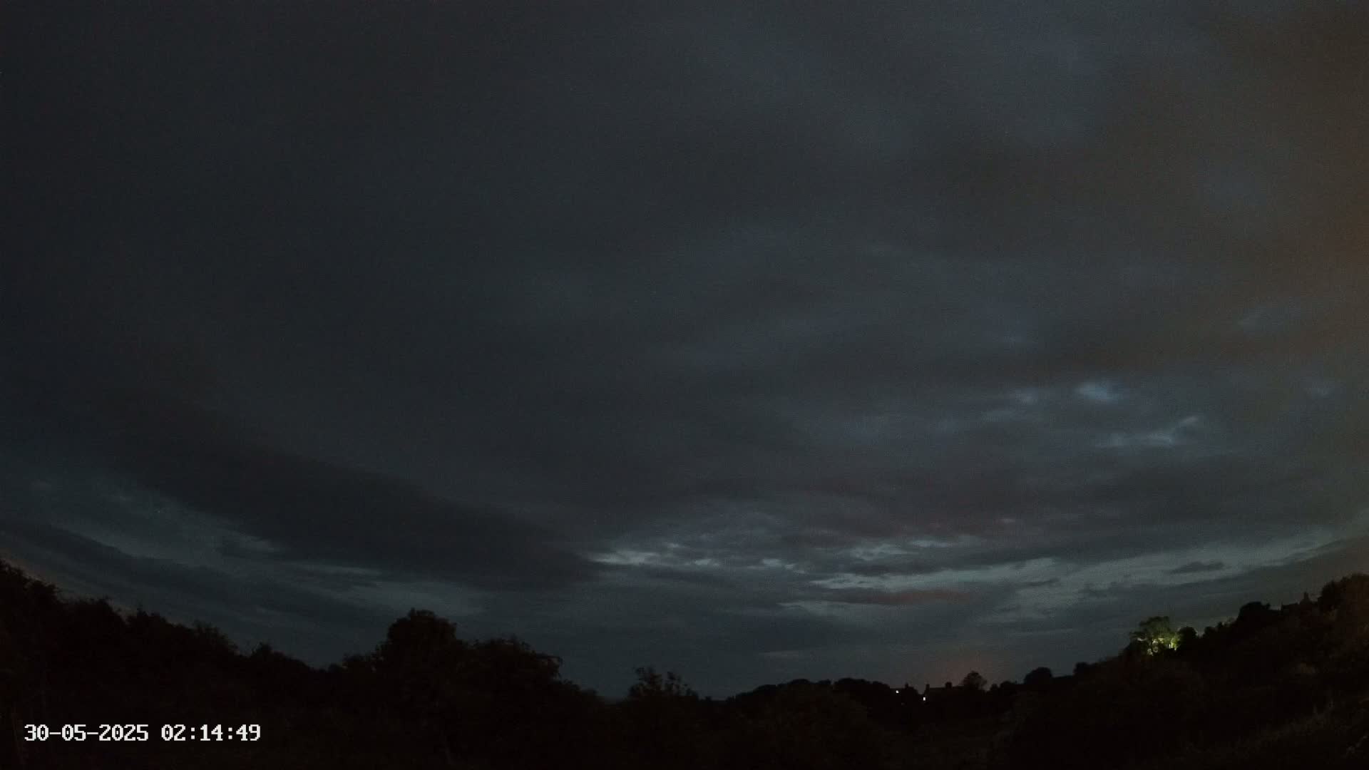 A dark, cloudy night sky over a silhouetted treeline.