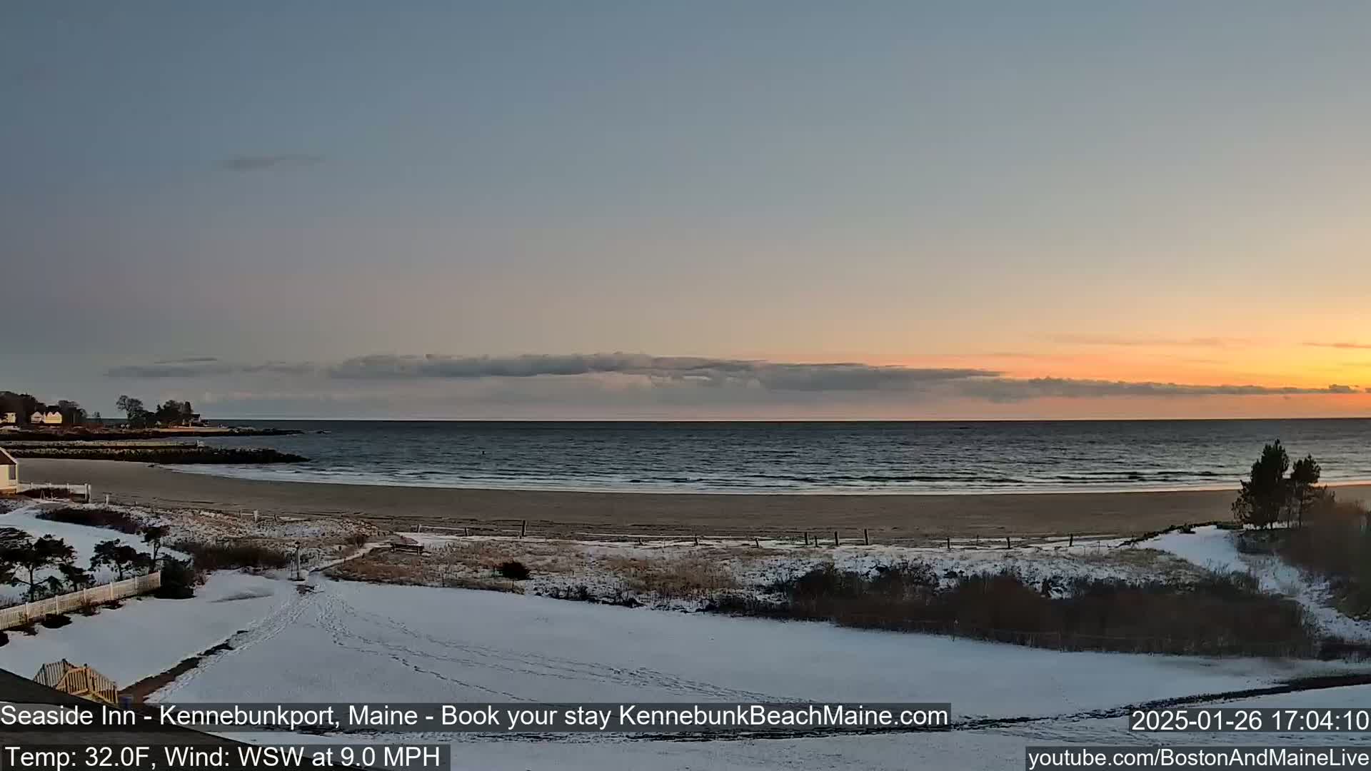 A snowy beach with a calm ocean under a sunset sky.