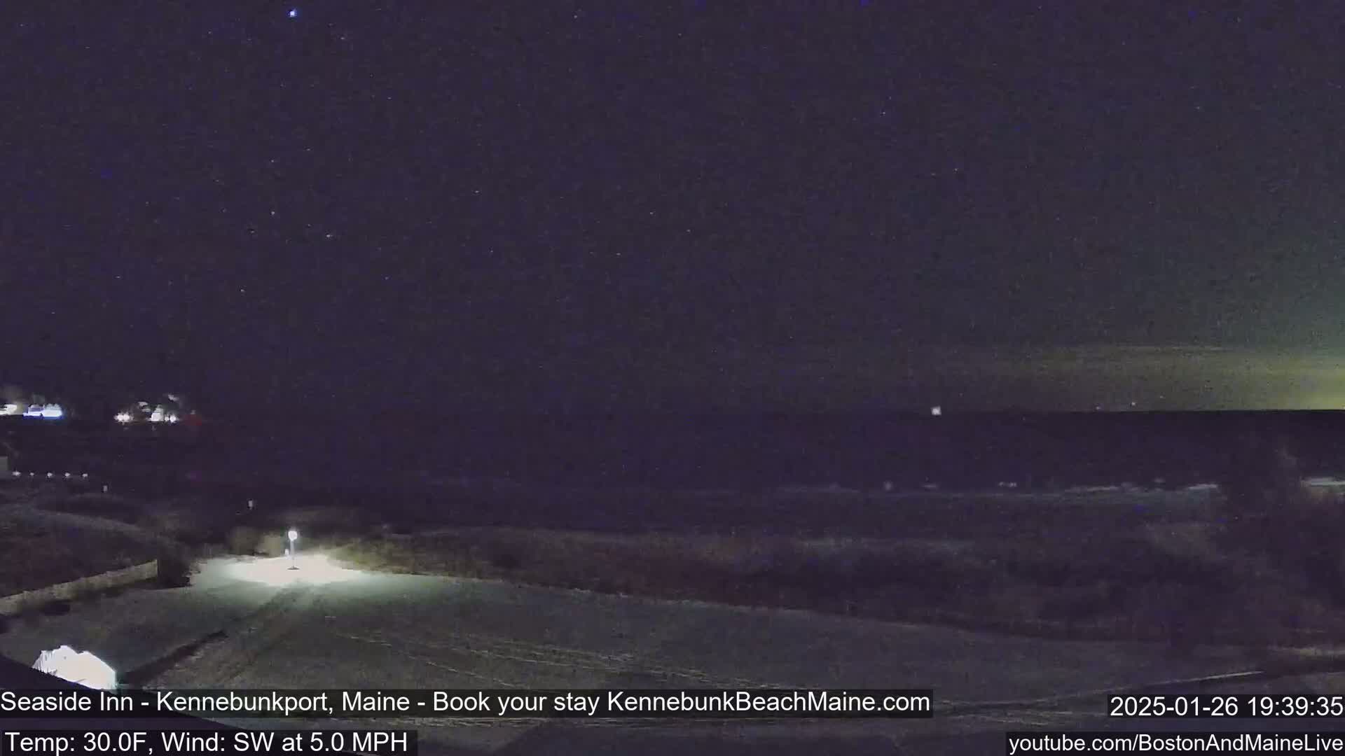 A nighttime view of a snow-covered landscape near a dark ocean under a clear, starry sky.