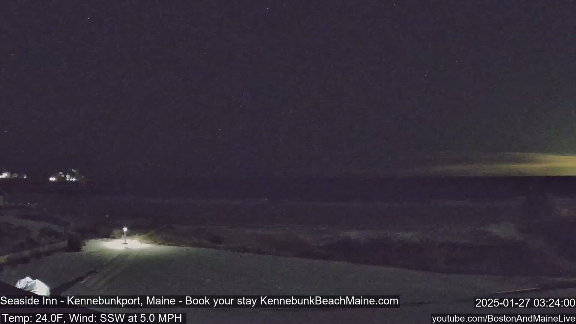 A nighttime, snowy scene overlooking a dark ocean under a clear, starry sky.