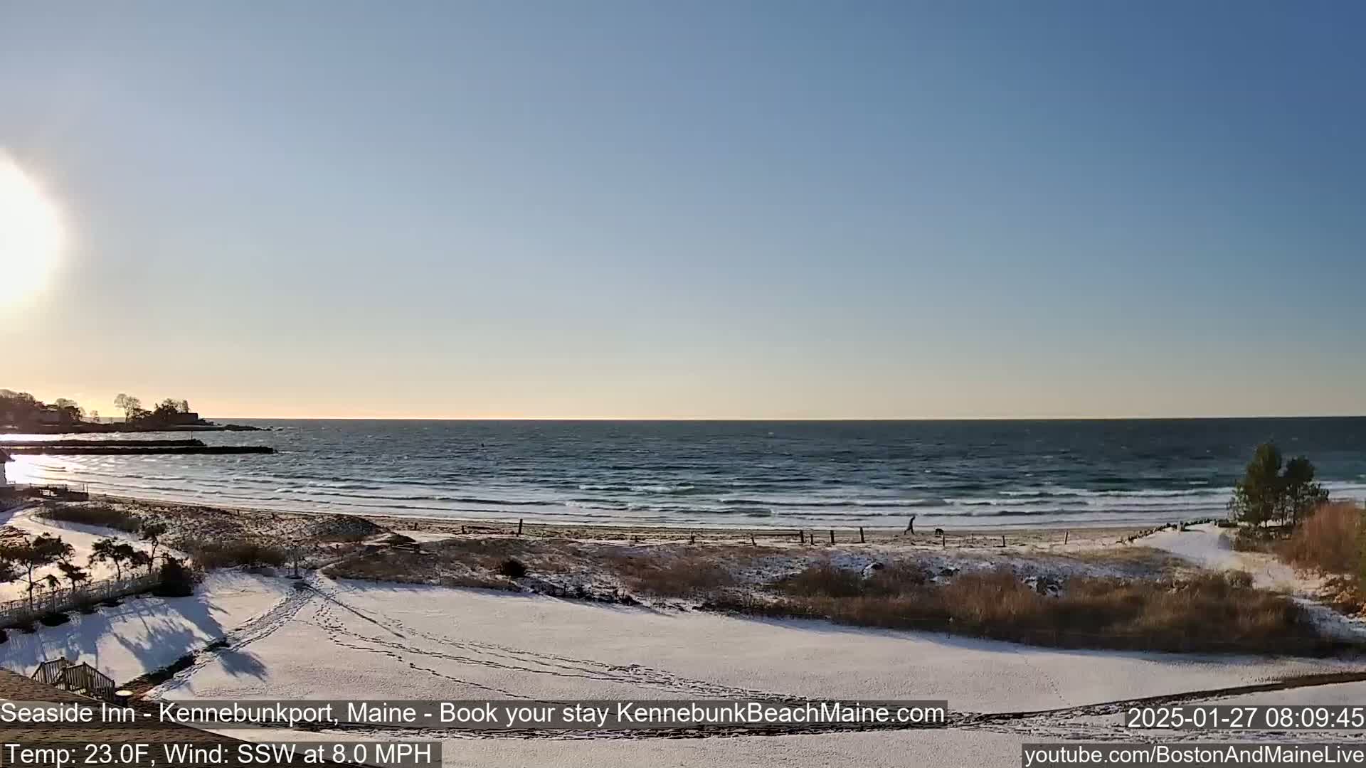 A snow-covered beach scene with a calm ocean under a clear, bright sky.