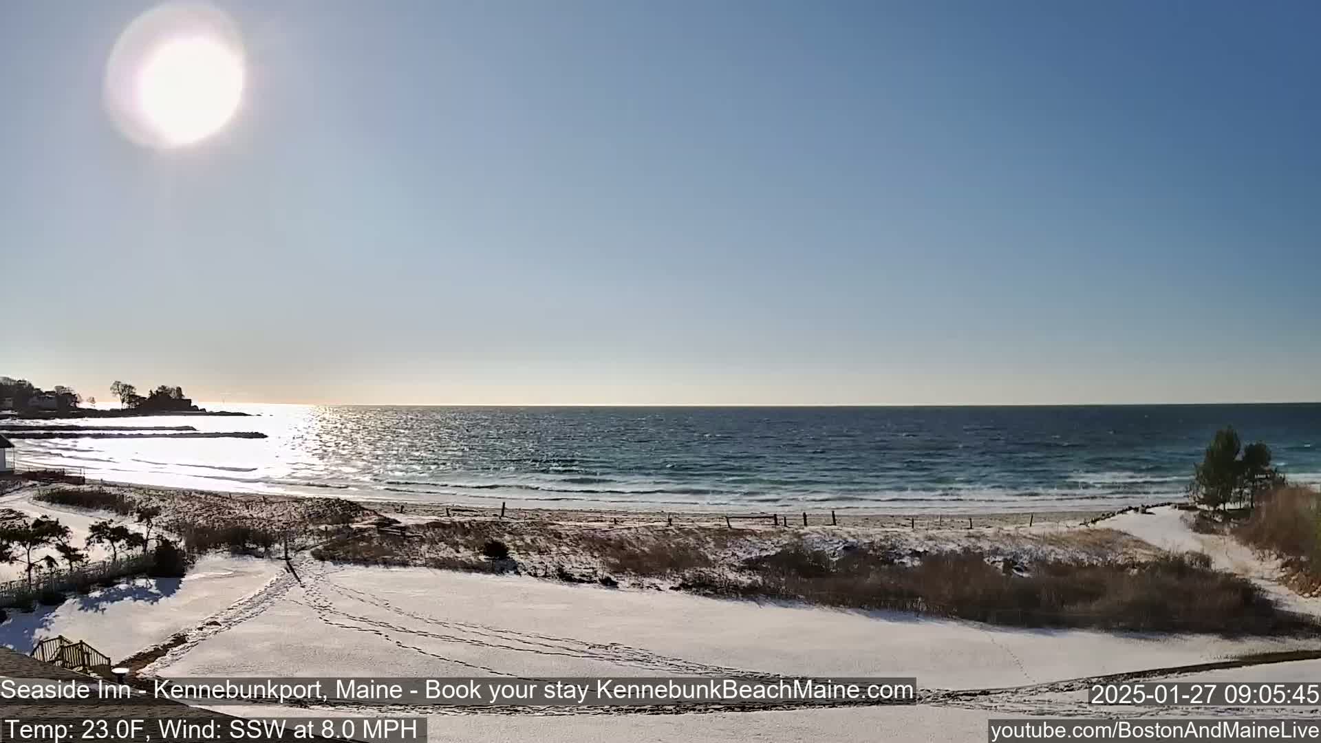 A sunny, cold day at a snow-dusted beach shows a calm ocean meeting the shore.