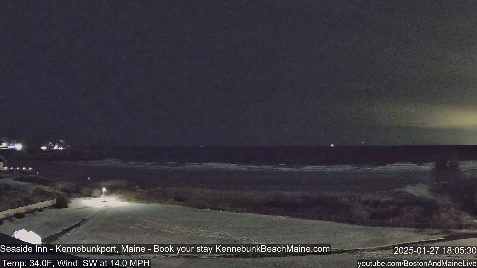 A snow-covered coastal area at night shows a dark ocean with small waves under a dark sky.