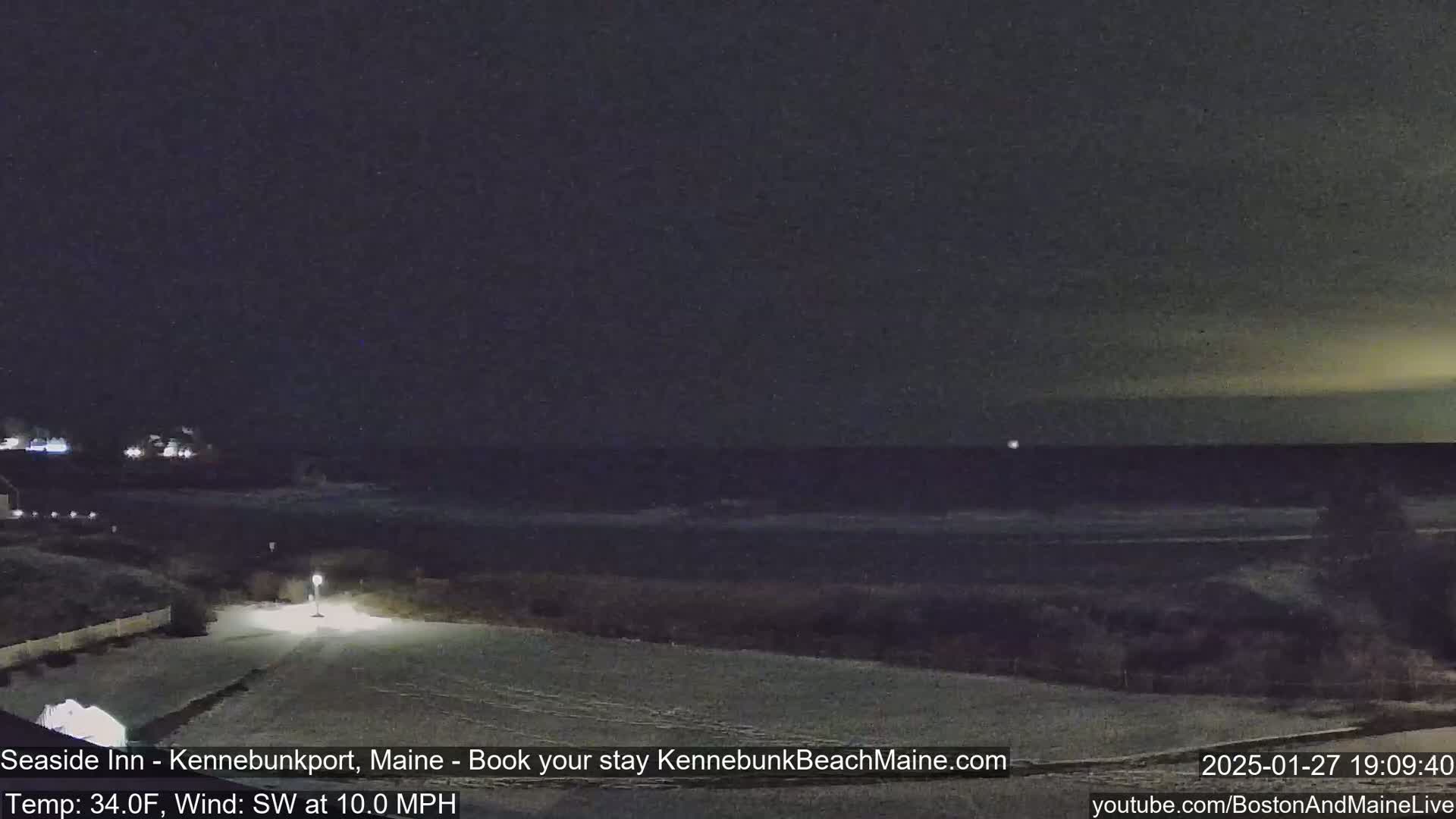 A snow-covered landscape at night shows a dark ocean under a mostly clear, yellowish sky with a southwest wind.