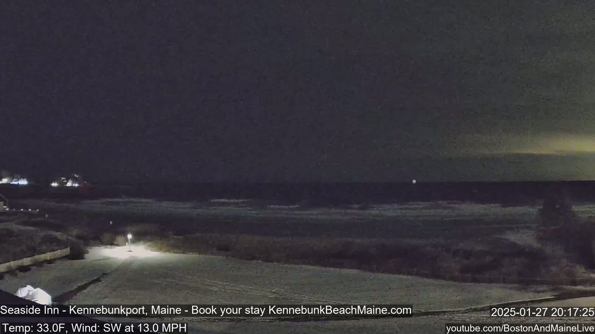 A nighttime view of a snow-covered beach with a dark, wavy ocean under a mostly clear sky.