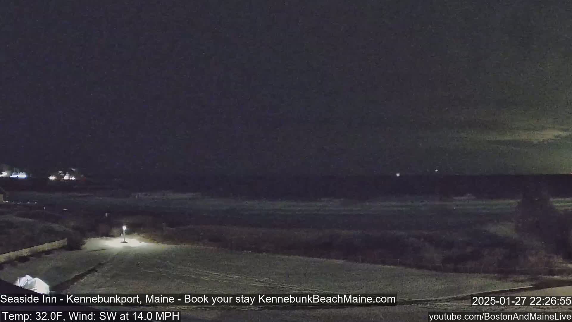 A nighttime view of a snow-covered beach and a roadway leading to it, under a dark sky with a slight wind.