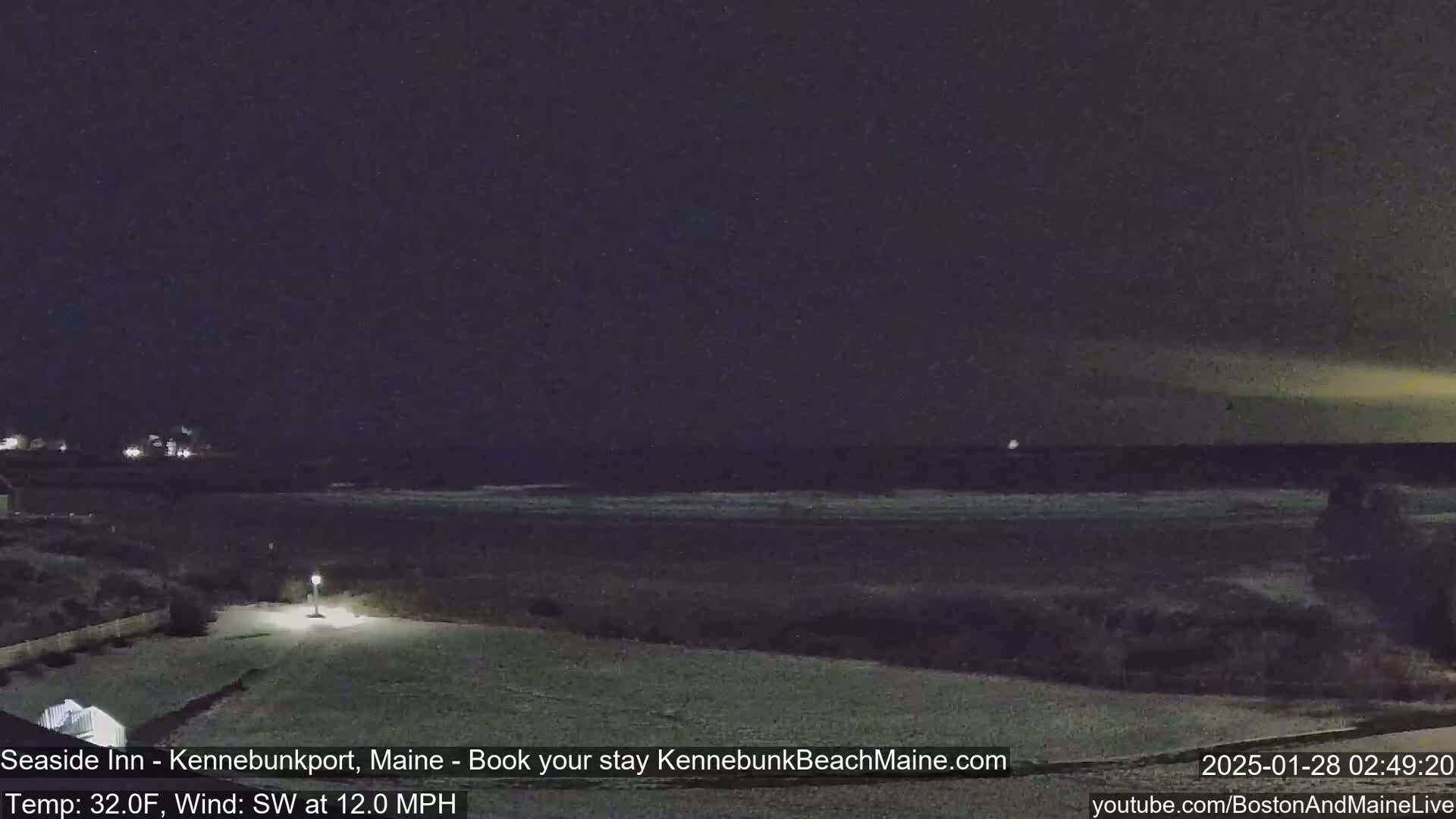 A nighttime view of a snow-covered beach with a calm ocean under a dark sky.