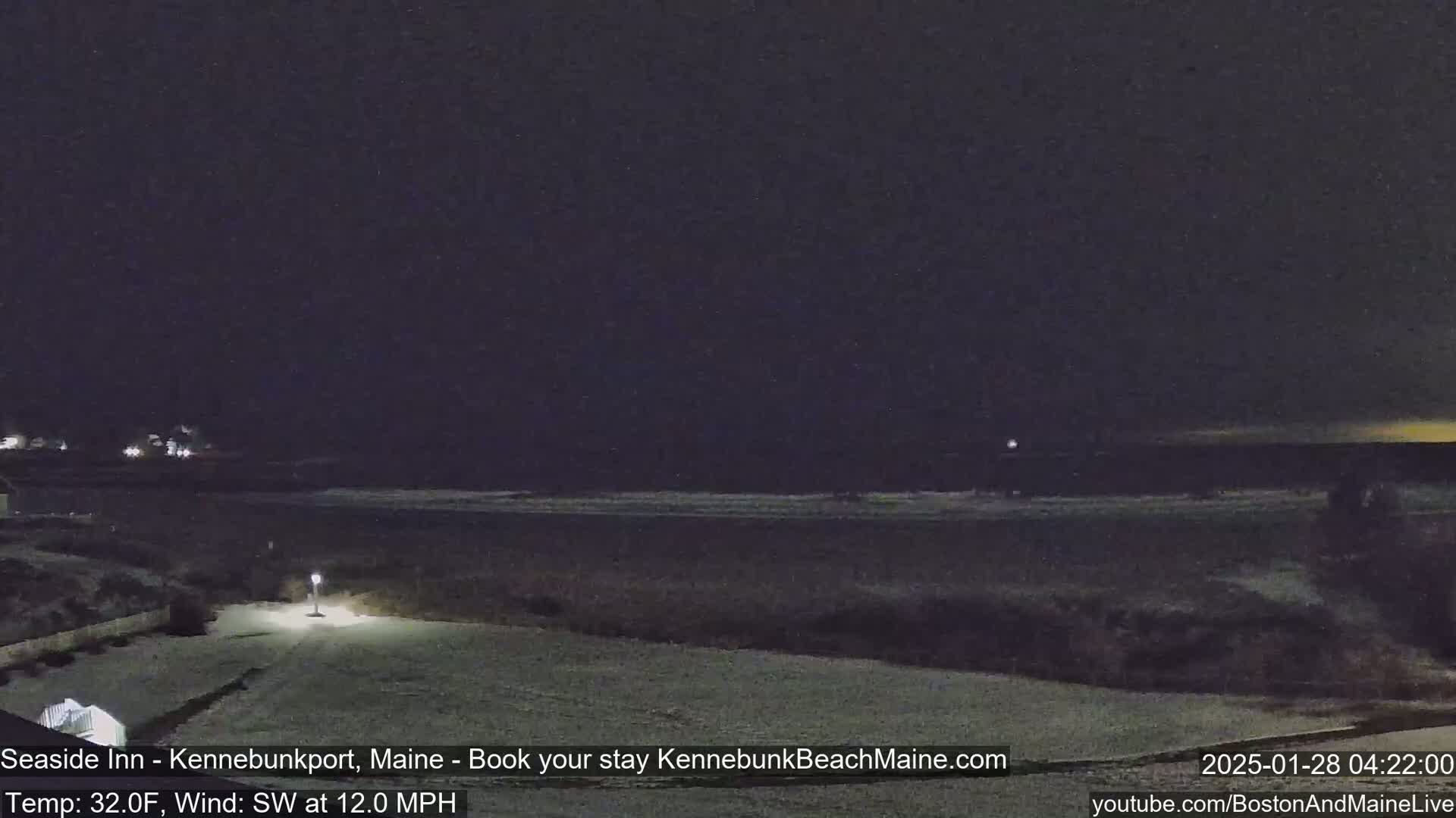 A snow-covered landscape at night shows a dark ocean with small waves under a mostly clear, dark sky.