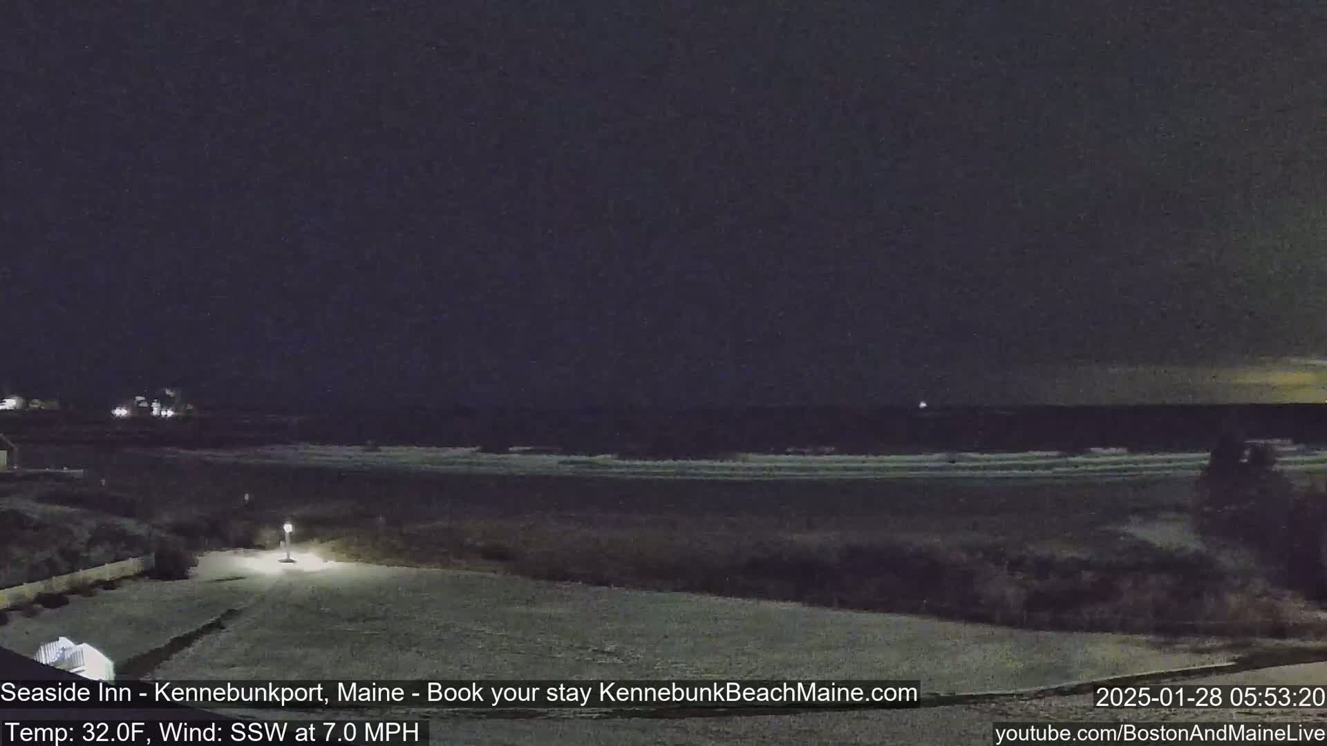 A snow-covered landscape at night shows a dark ocean with small waves under a dark sky.