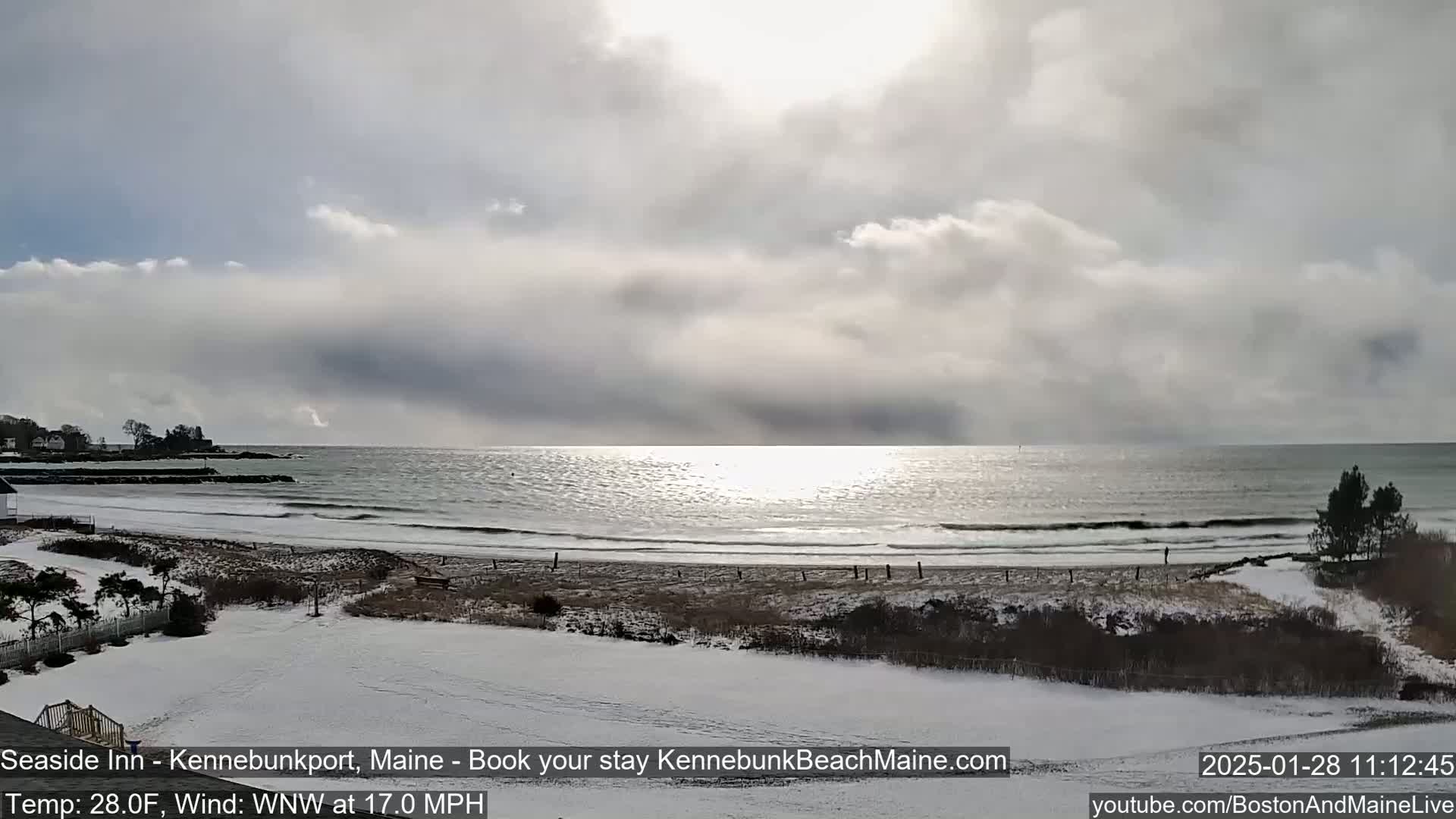 A snow-covered beach with a calm ocean under a cloudy sky.