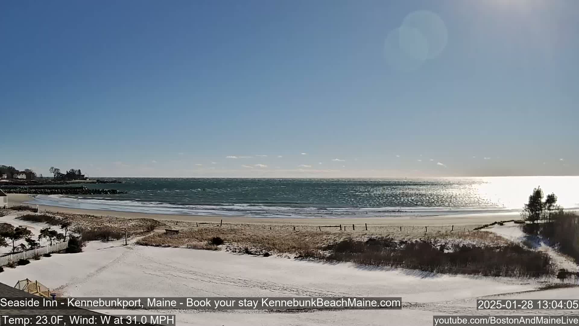A snowy beach with a windy, wavy ocean under a clear blue sky.
