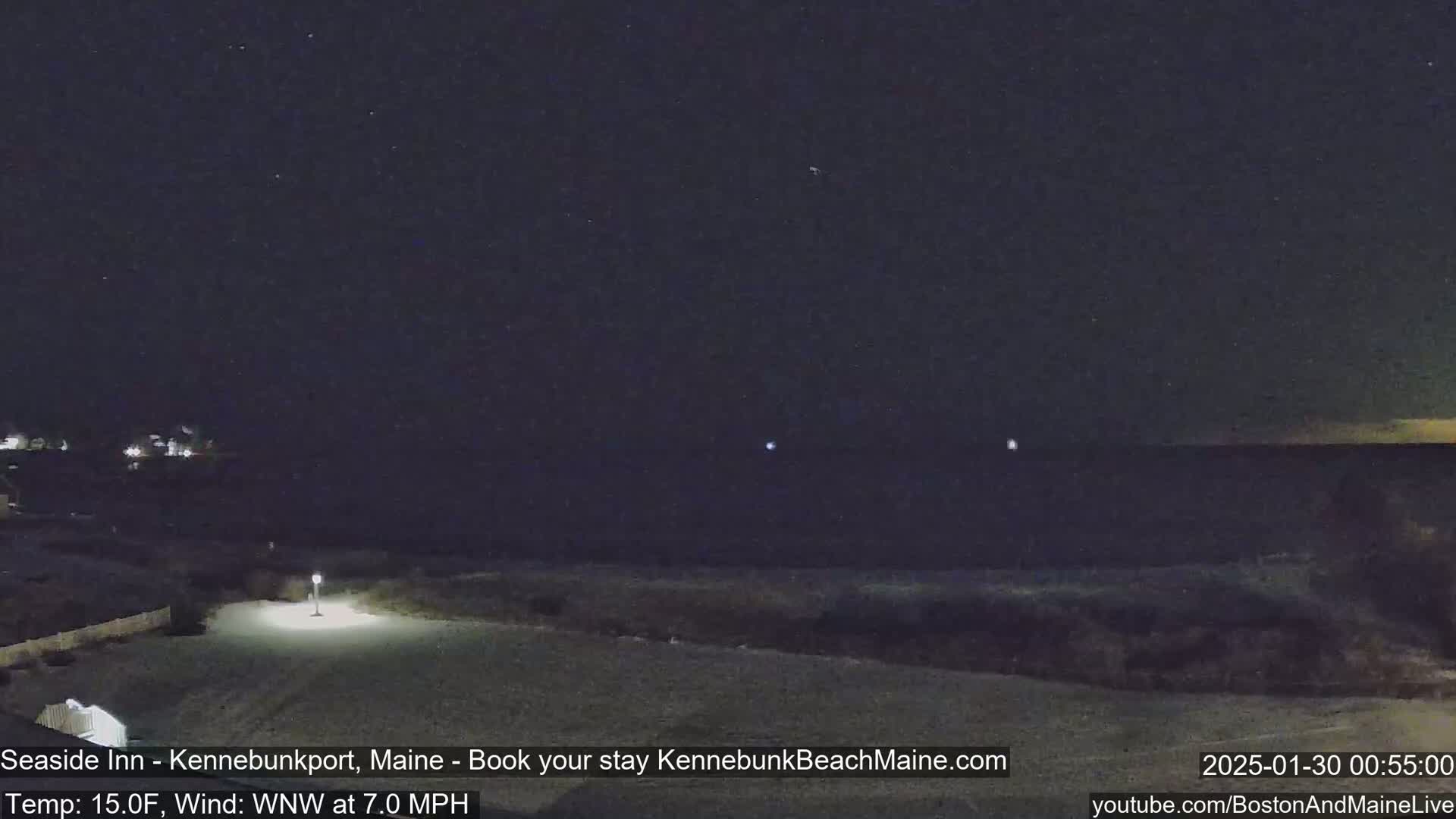 A nighttime view of a dark beach and ocean under a clear, starry sky with a gentle wind.