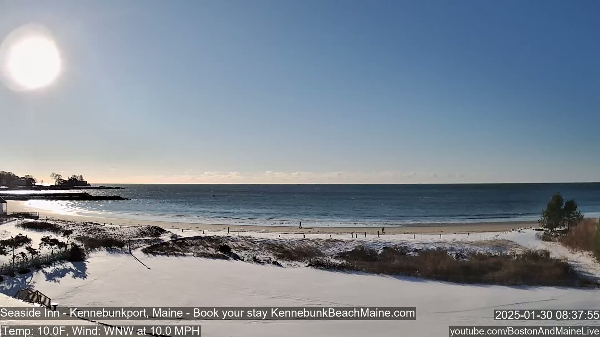 A snow-covered beach with a calm ocean under a bright, sunny sky.