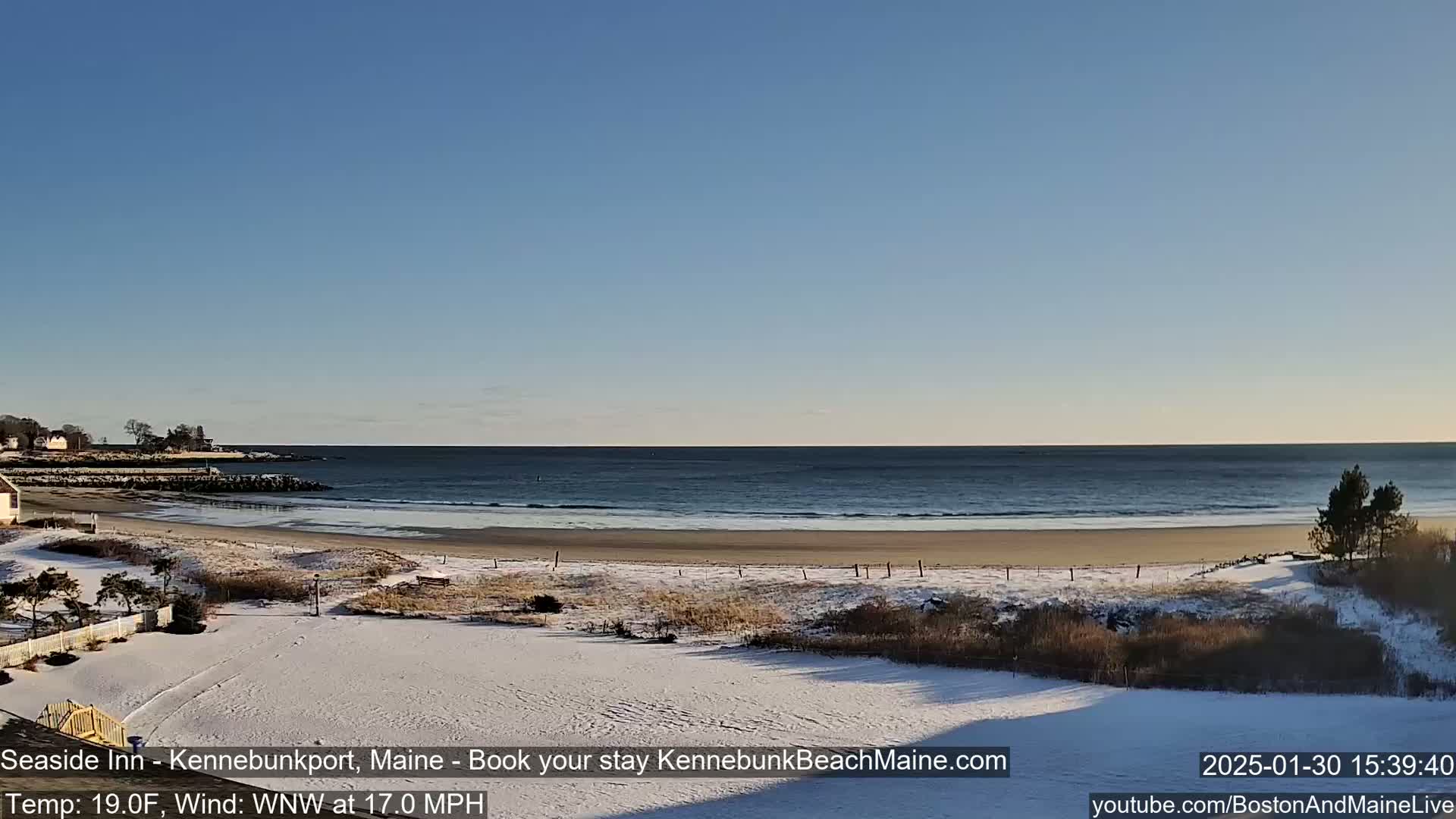 A snow-covered beach with a calm ocean under a clear blue sky.