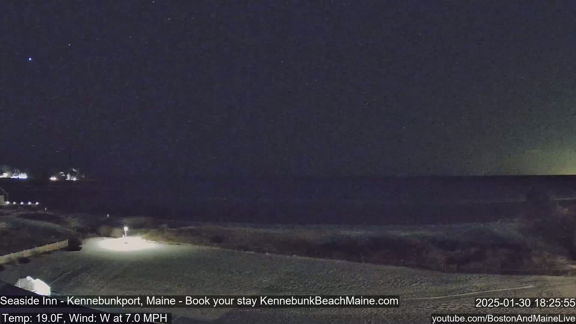 A nighttime view of a dark ocean under a clear, starry sky with a calm, sandy shore in the foreground.