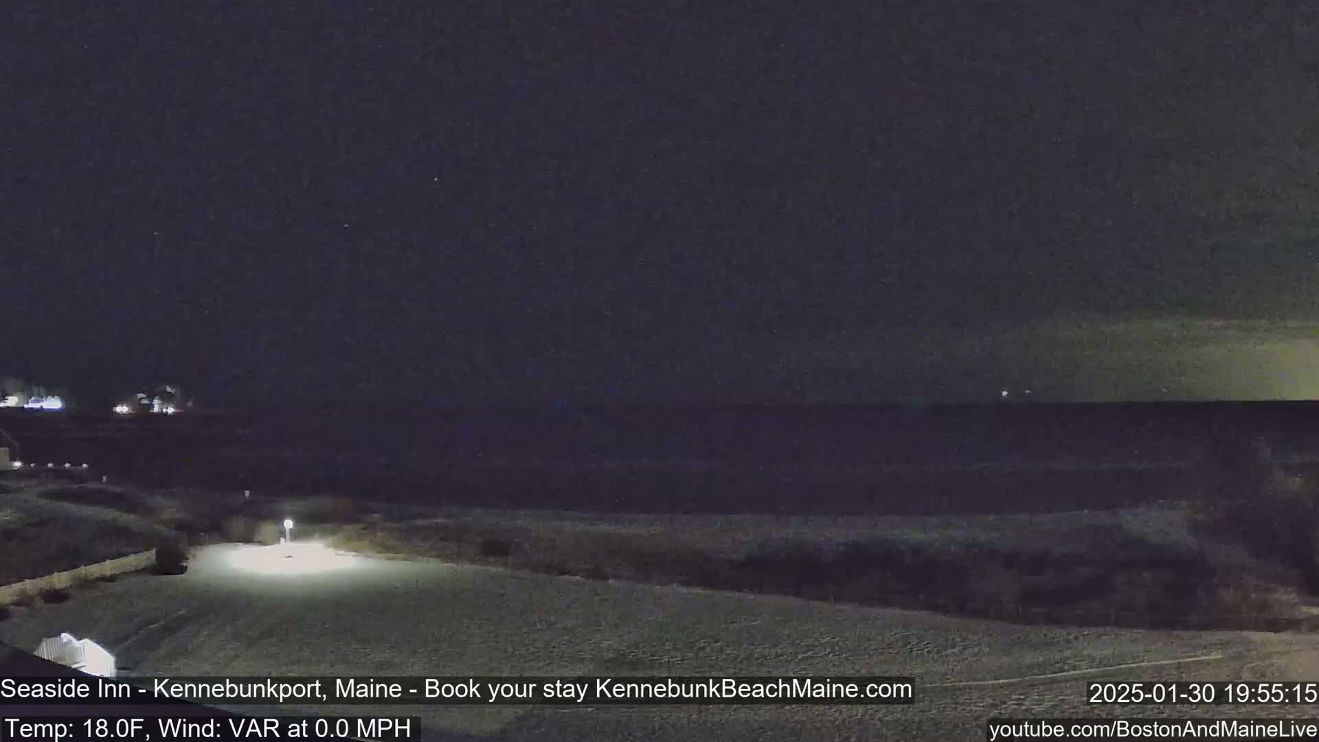 A nighttime view of a snow-covered beach and ocean under a dark, clear sky.