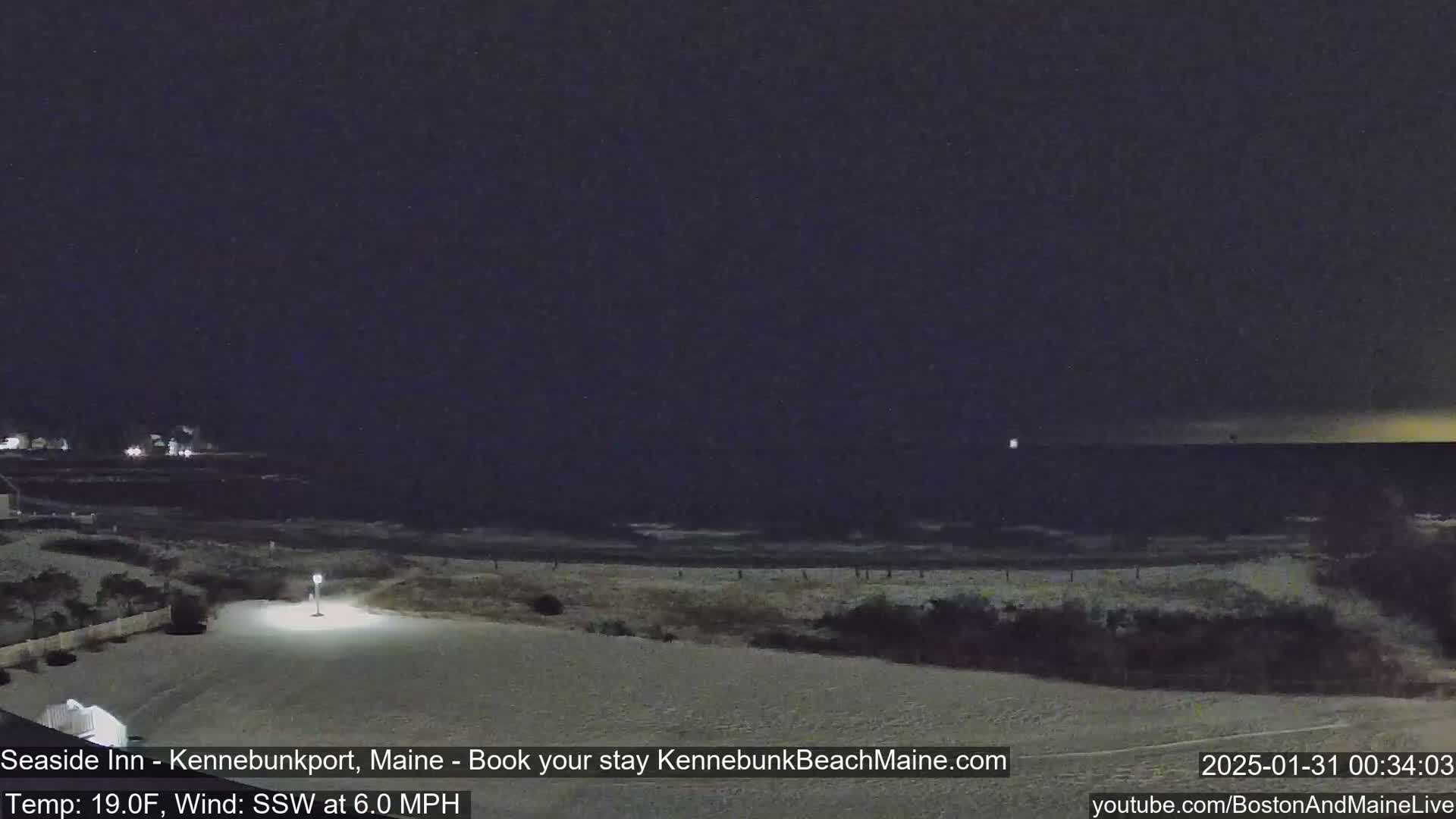 A nighttime view of a snow-covered beach with a dark, clear sky and a gently lapping ocean under a 19°F temperature and a 6.0 mph south-southwest wind.