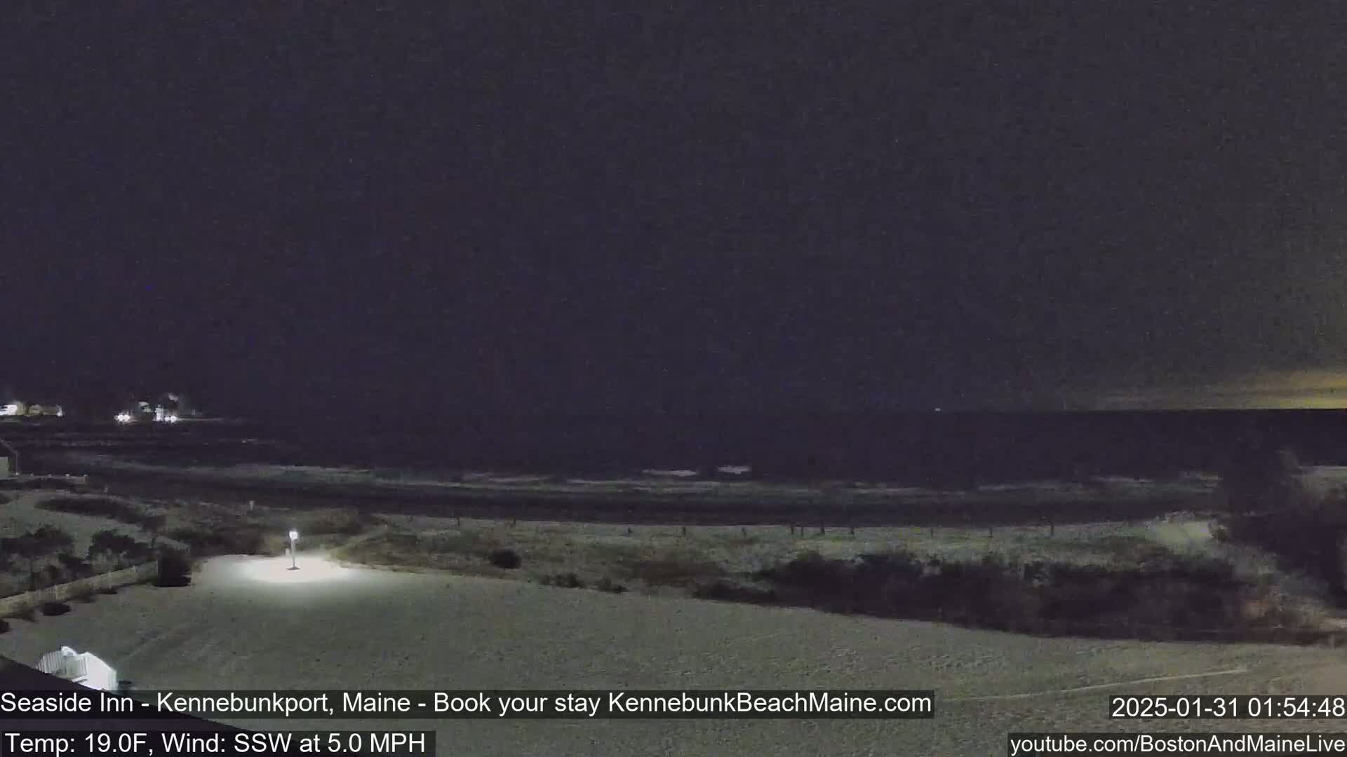 A snow-covered beach at night with a dark ocean and a single lamp illuminating a small area of land.