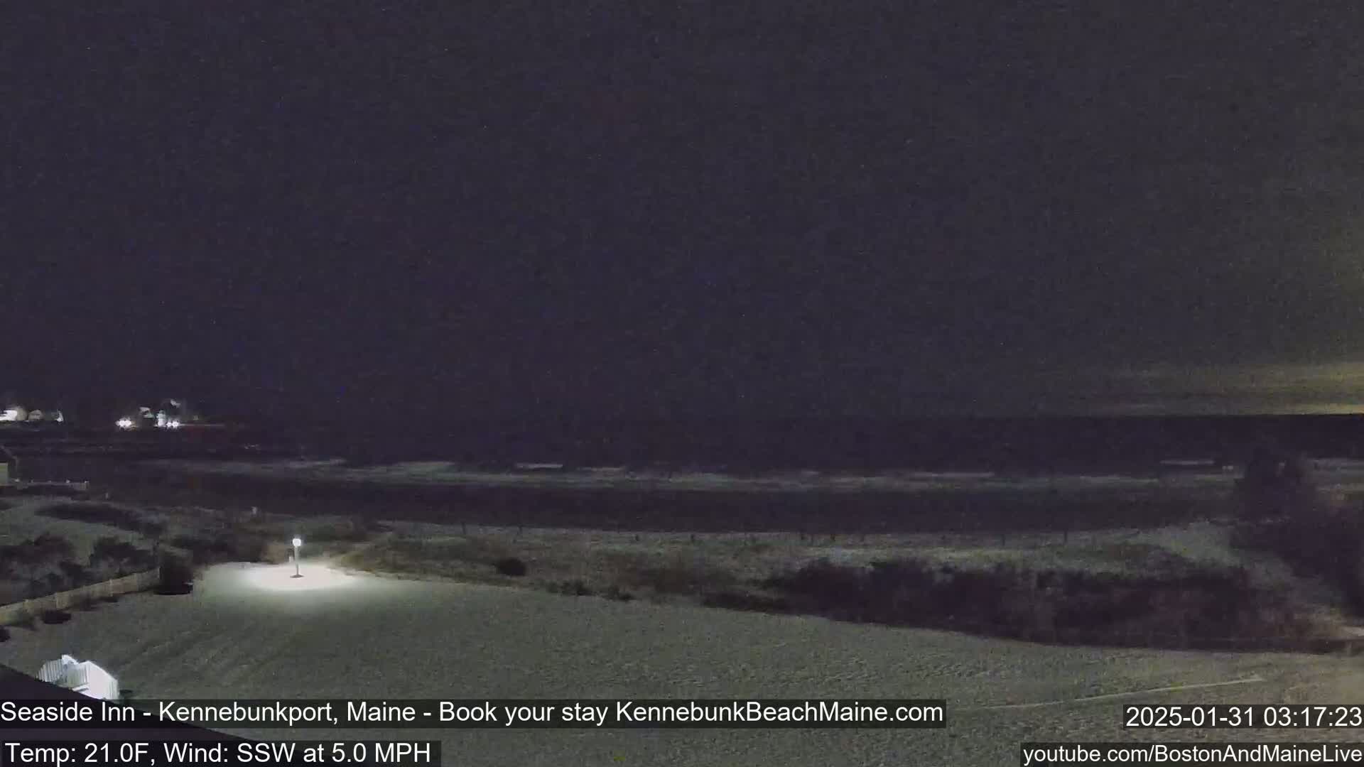 A snow-covered beach at night with a dark, calm ocean and a single lit lamppost.