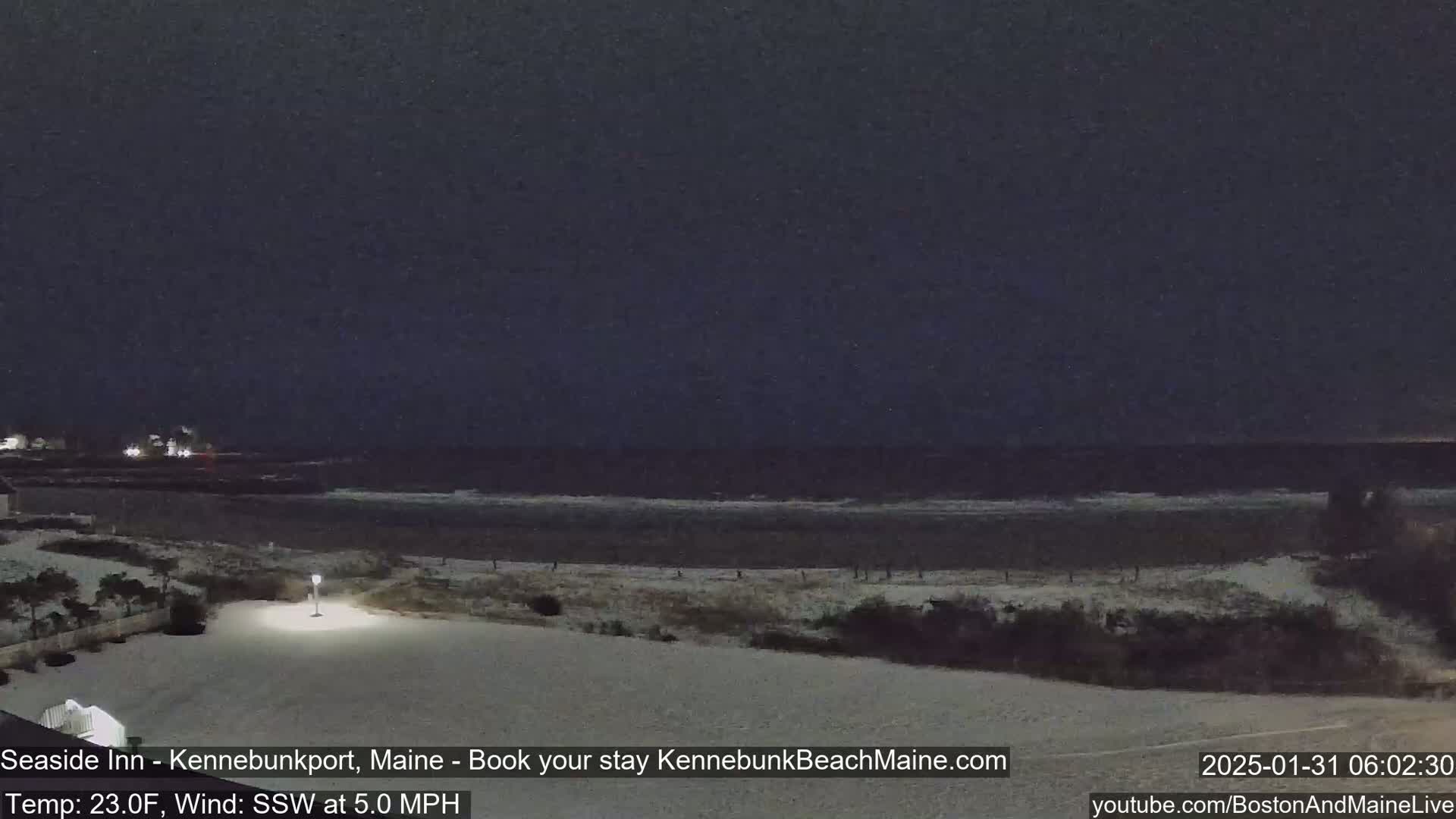 A snow-covered beach at night shows a dark ocean with small waves under a dark sky.